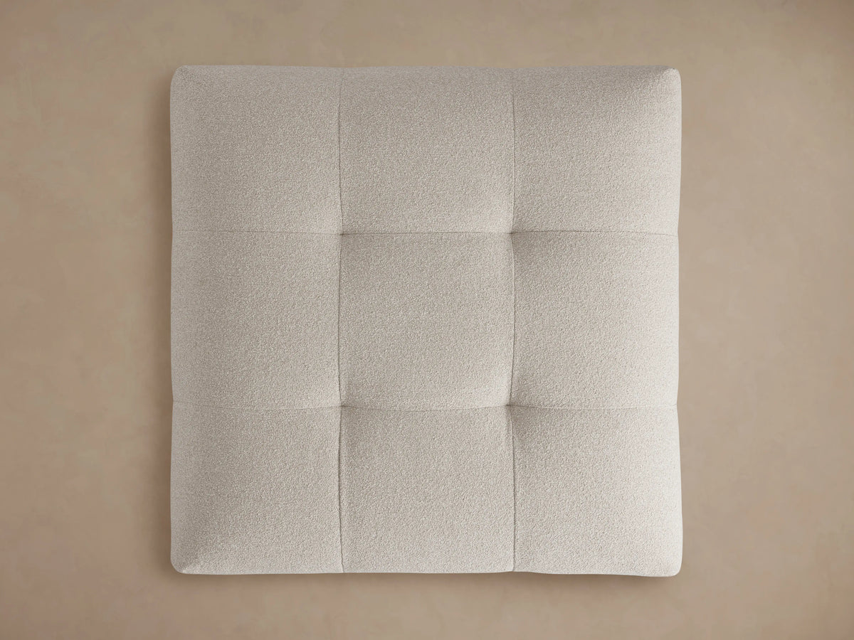 Close-up of a light beige, textured, tufted Keegan Ottoman, showing soft corners and woven fabric details from above.