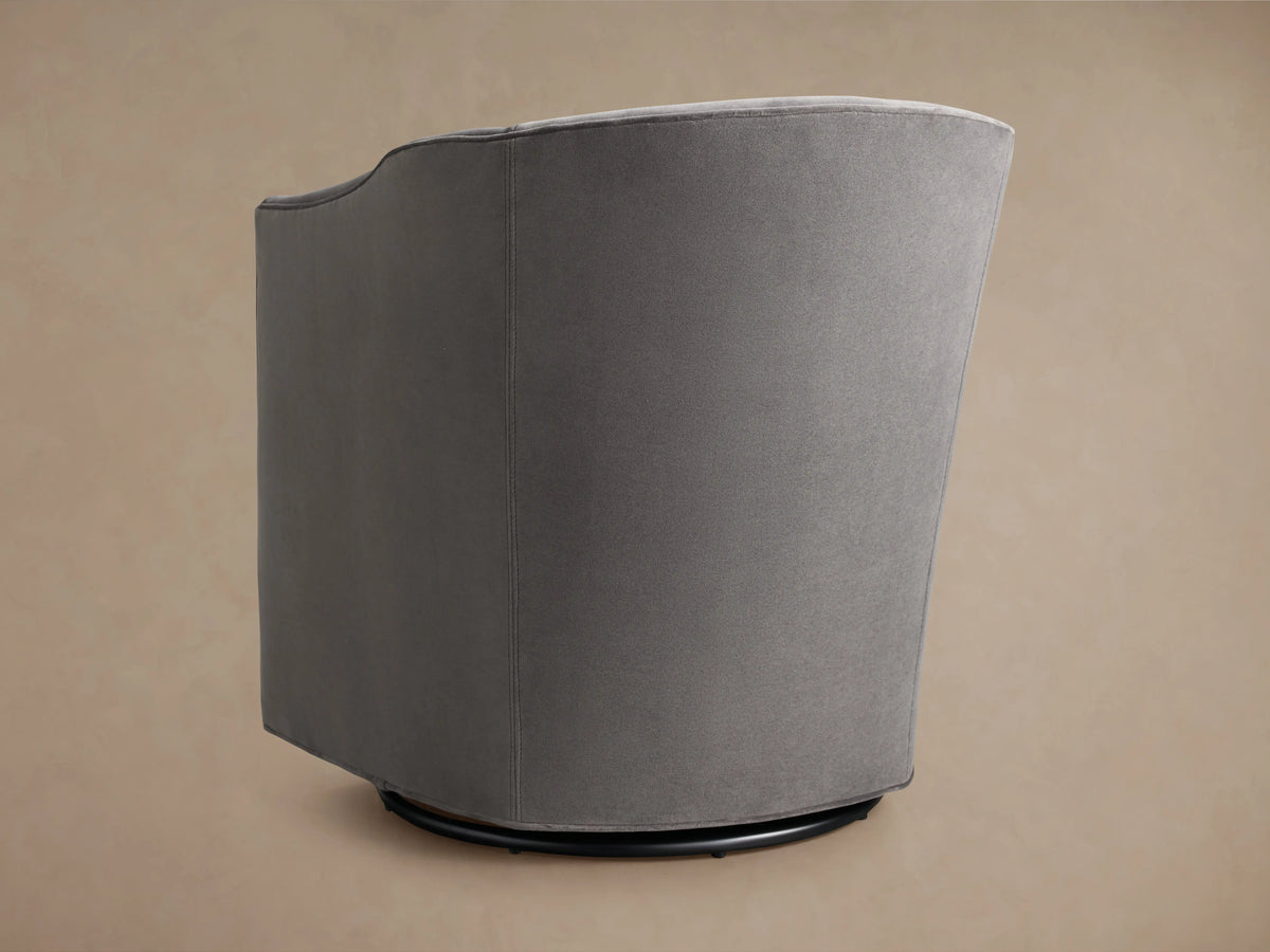Giles Swivel Chair in grey fabric featuring a smooth, curved backrest and armrest. The upholstery has a soft, velvety texture.