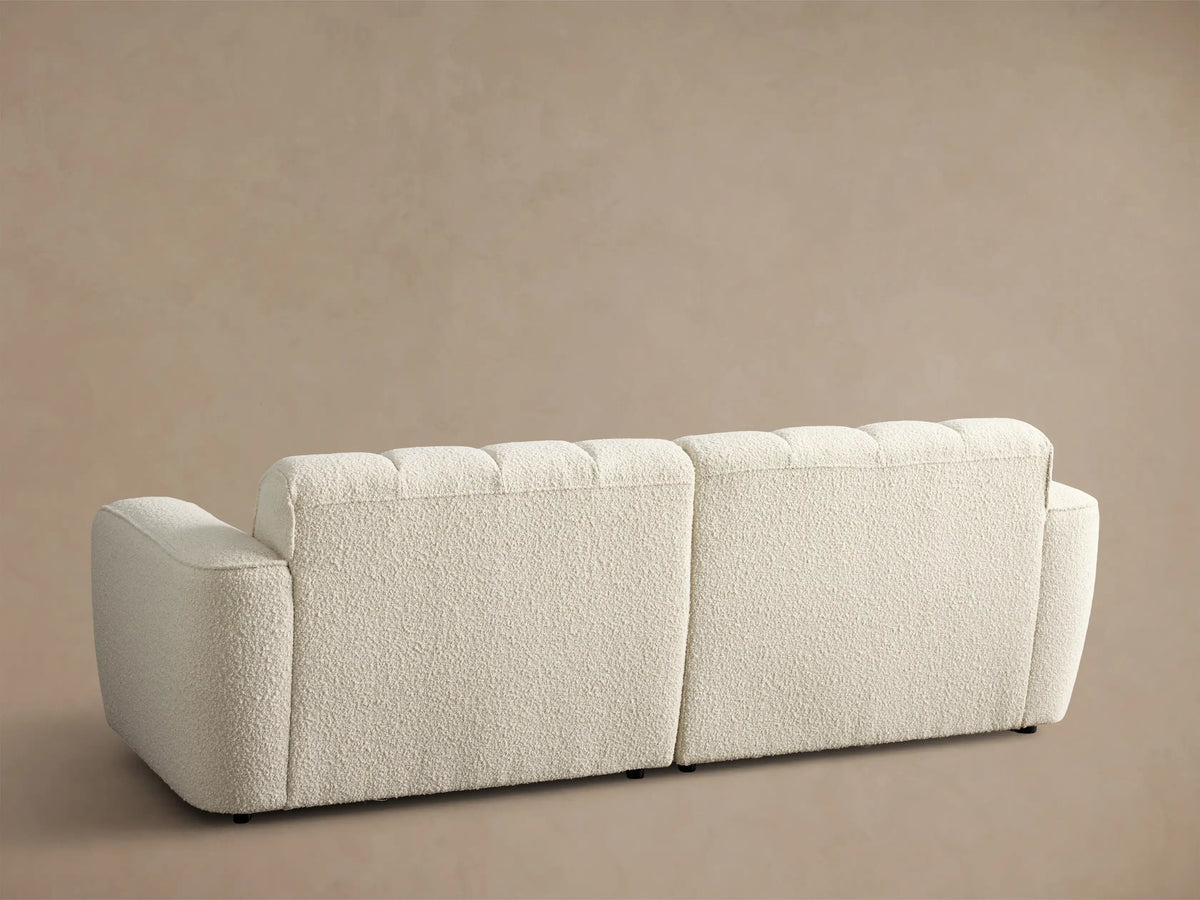Close-up of the cream Bracco Two-Piece Sofa, featuring textured fabric, vertical channel tufting, and a curved armrest.