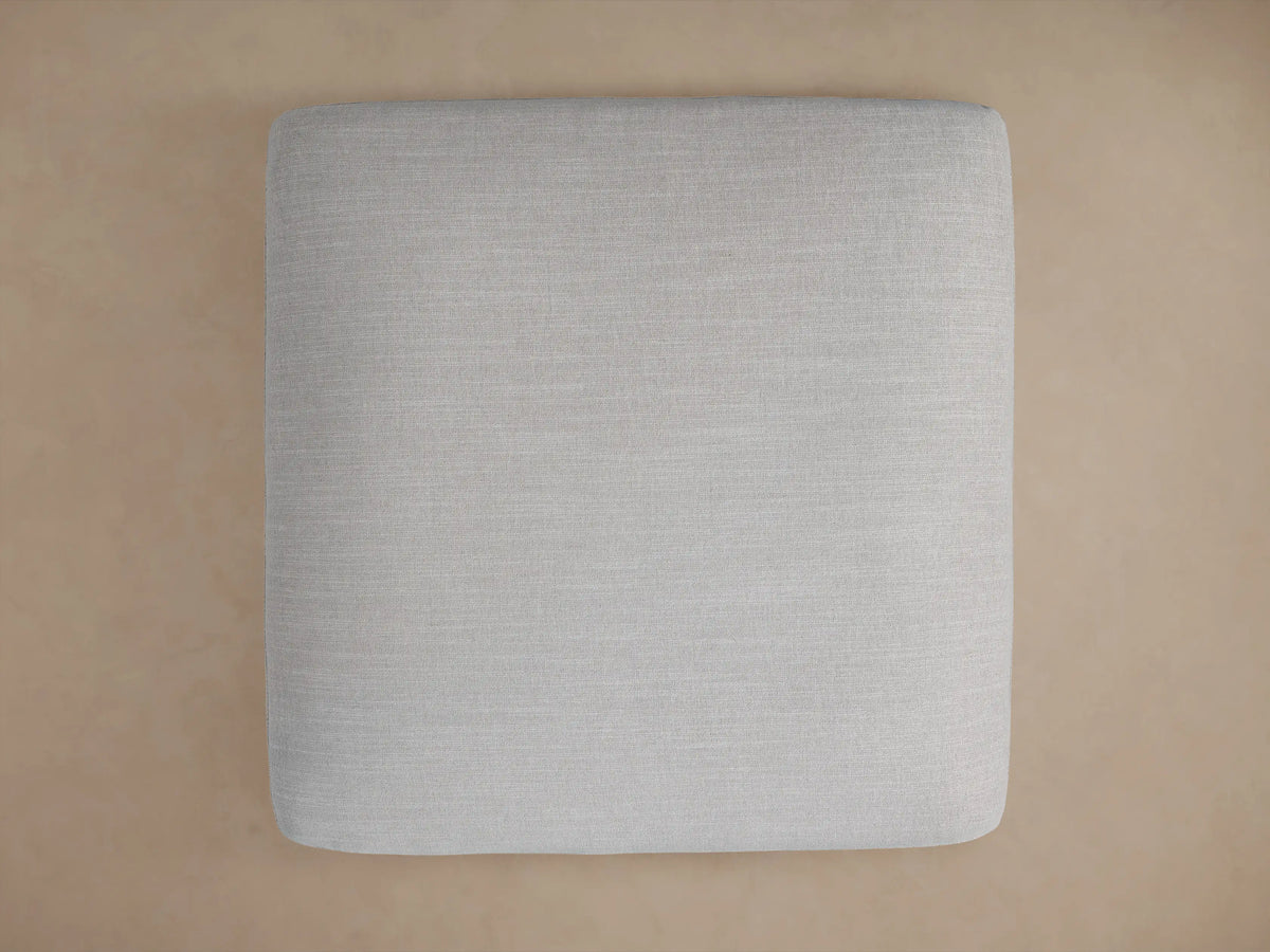 Close-up of a Duncan Ottoman upholstered in light gray fabric, showing the woven texture and a neatly sewn corner.