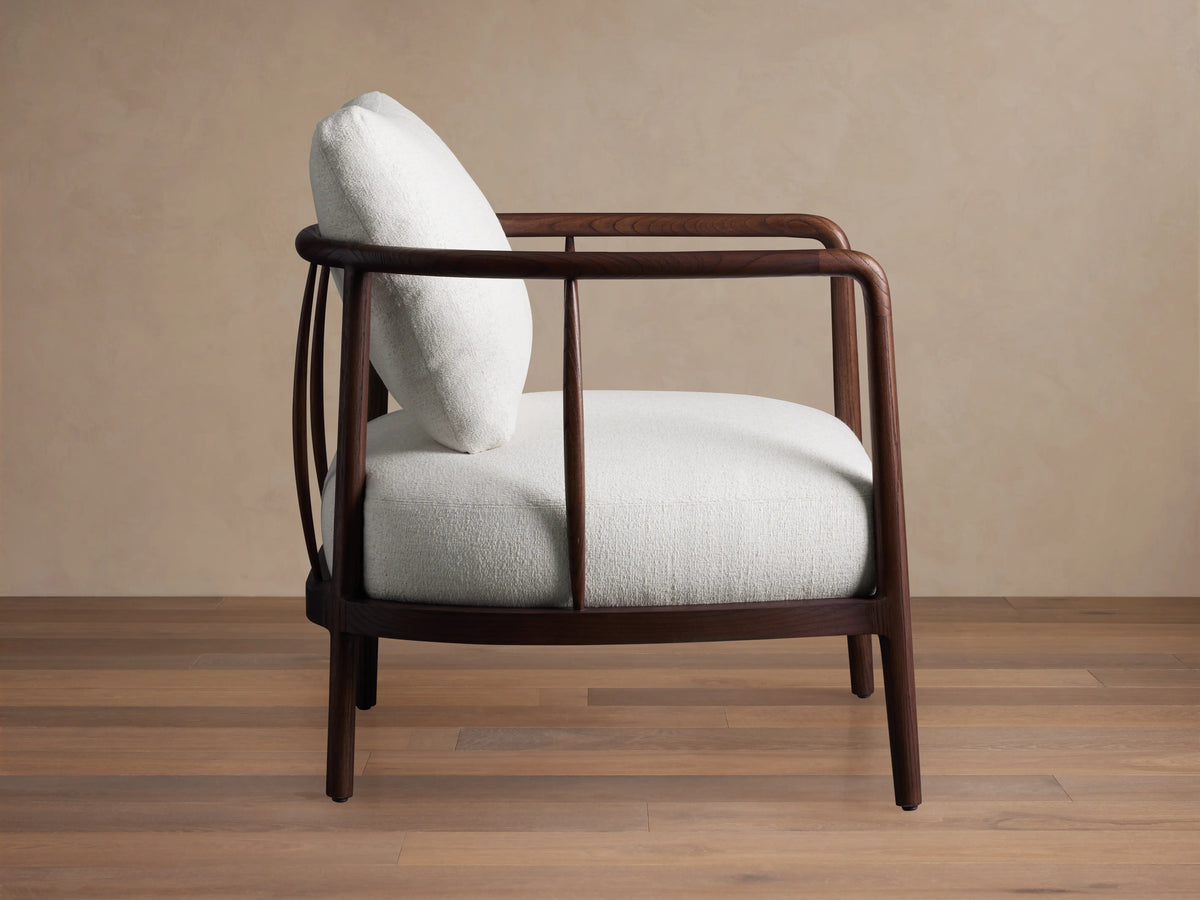 Alt text: Griggs Chair with a curved wooden frame in rich mahogany tones, featuring lightly colored plush upholstery and a cushioned backrest.