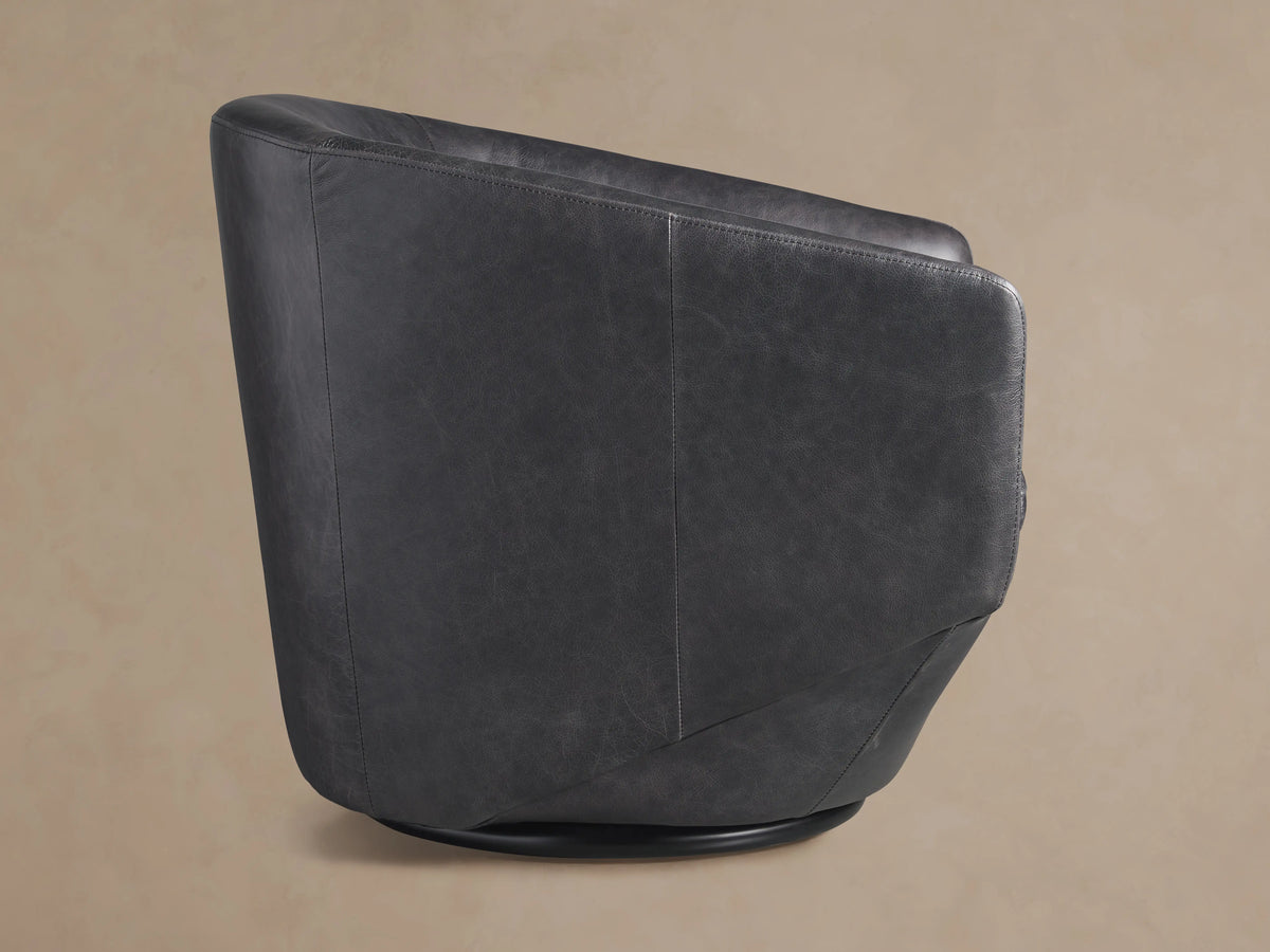 Close-up of Pelton Leather Swivel Chair's dark grey distressed leather seat, curved arm, and back with visible stitching.