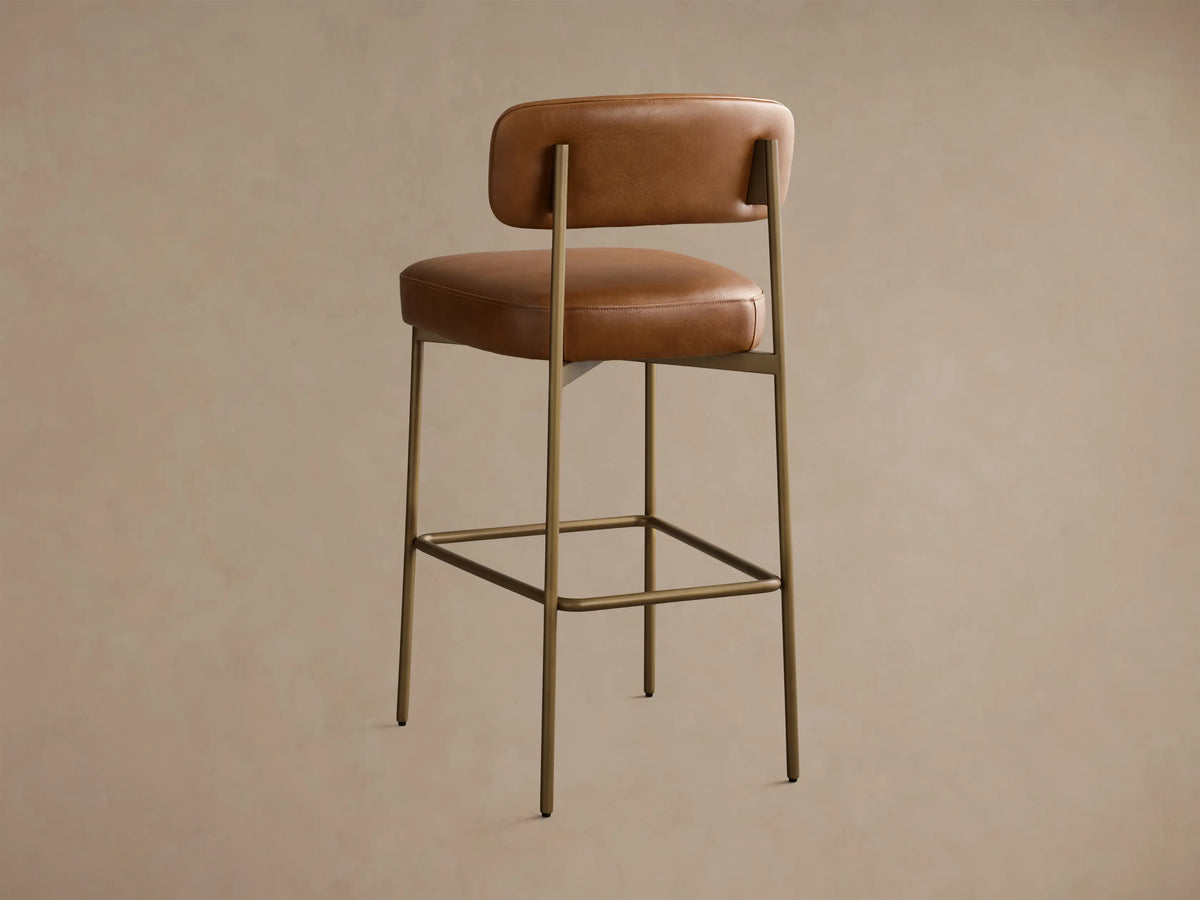 Close-up of the cognac leather chair back and seat with bronze frame detail and visible stitching.