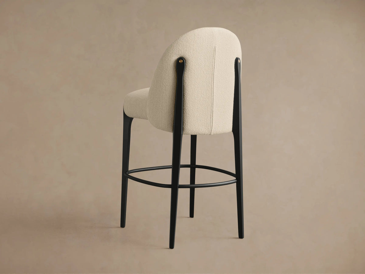 Close-up of Bottoni Stool's cream textured upholstery, black frame, and brass tack accent from a slightly elevated angle.