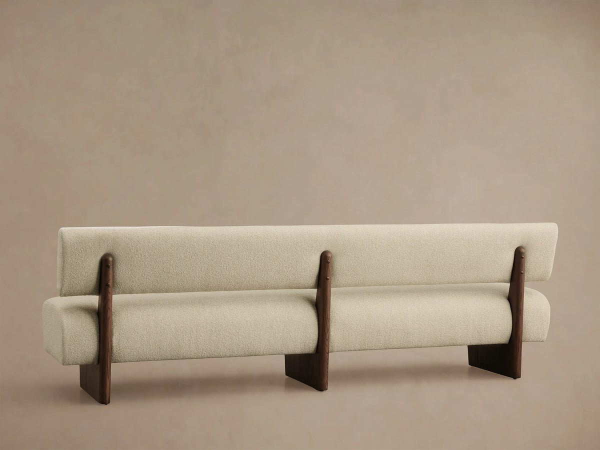 Beau Banquette with curved light cream textured fabric back and seat, supported by a dark wood frame detail.