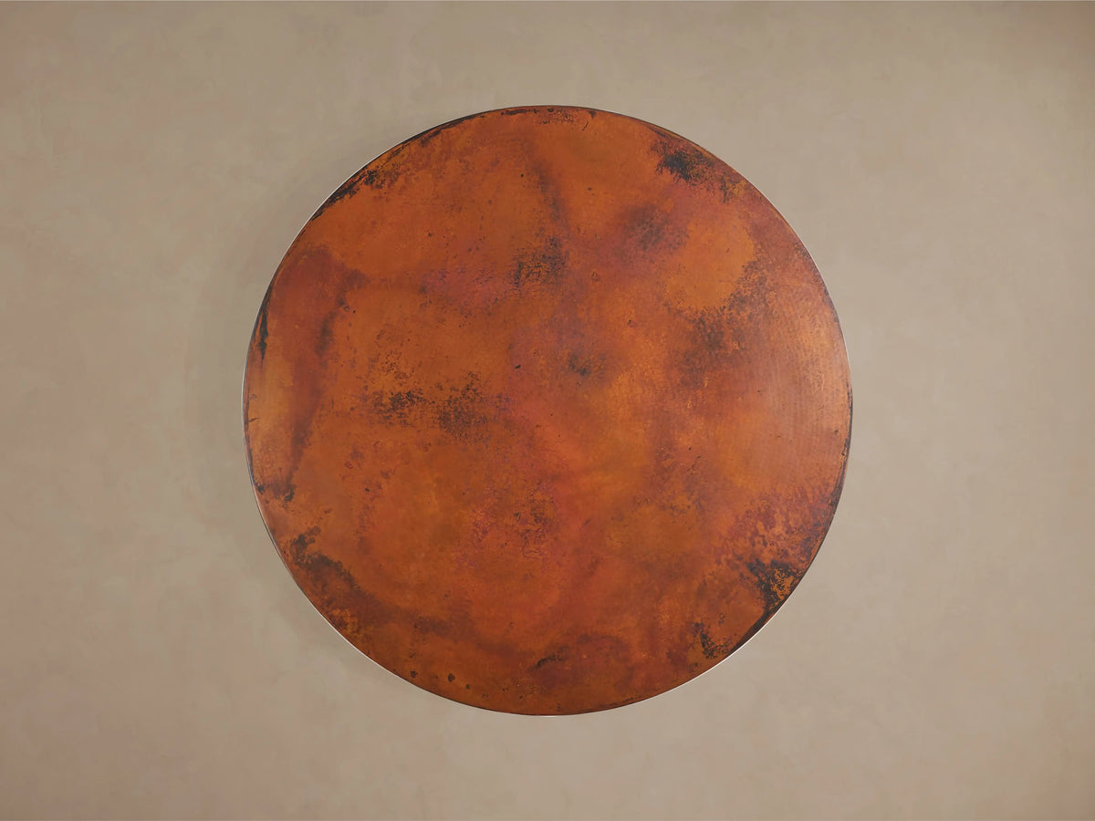 Recycled Metal Round Dining Table showing a detailed, hand-hammered copper tabletop with warm tones and a Monarch butterfly stamp on the edge.