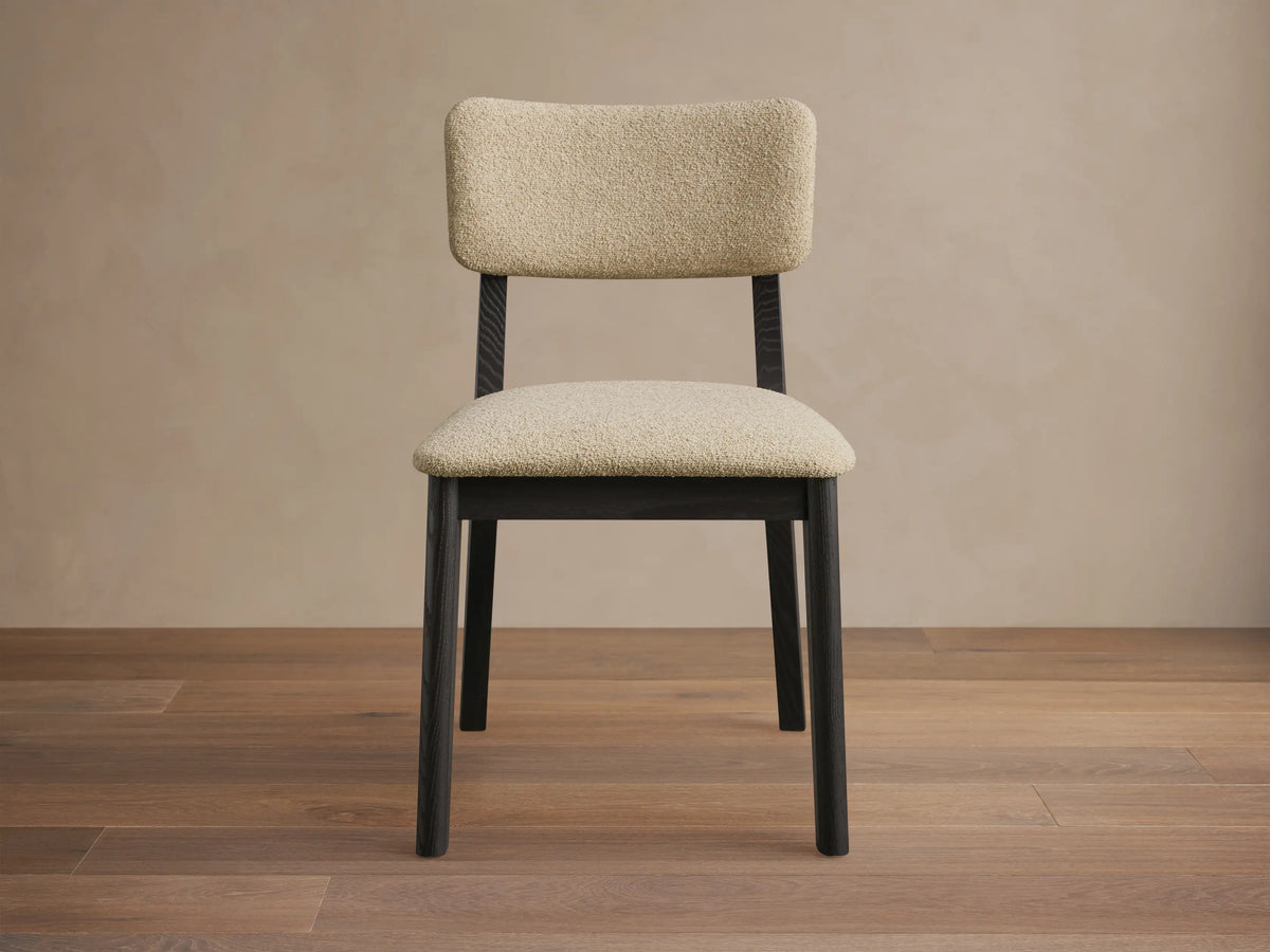 Close-up of the Corrado Dining Side Chair, featuring a dark wood frame with a curved back support and light beige textured upholstery.