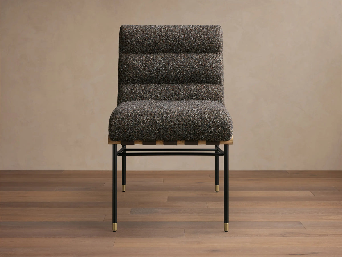 Side profile of a dark speckled upholstered lounge chair with a wavy backrest, black metal frame, and brass accents.