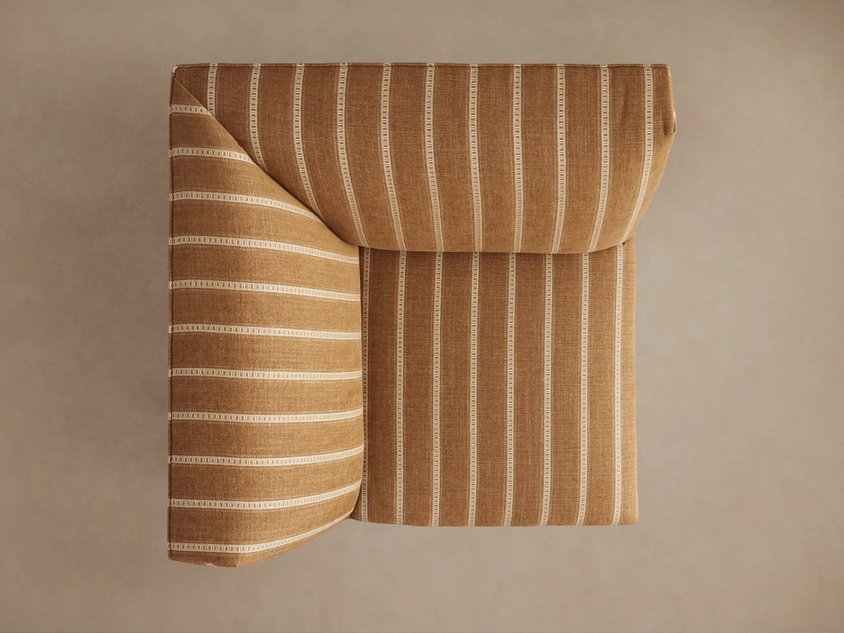 Eaton Corner chair upholstered in golden-tan fabric with white vertical pinstripes, standing on dark tapered legs, angled view.