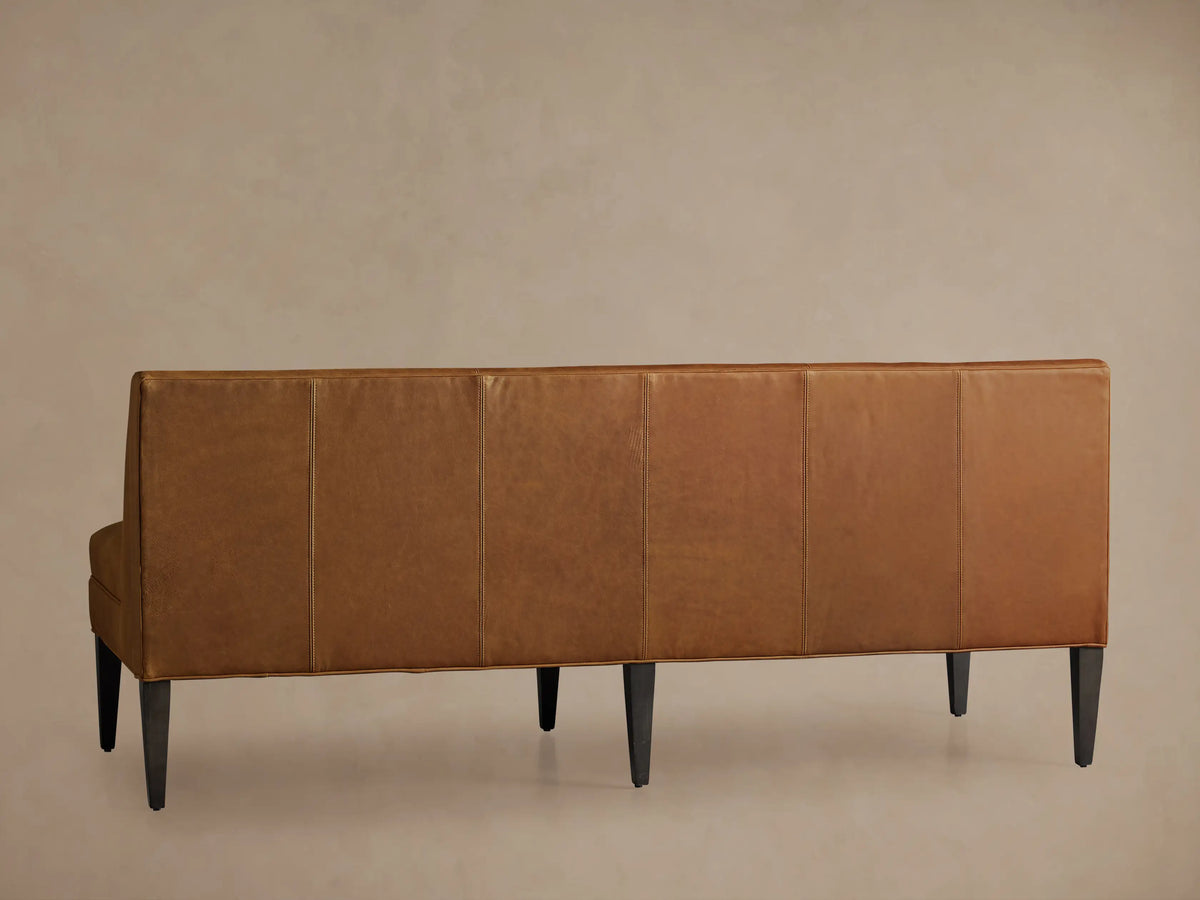 Close-up, angled view of the Gates Leather Settee, showing warm brown leather with vertical channel tufting on the backrest.