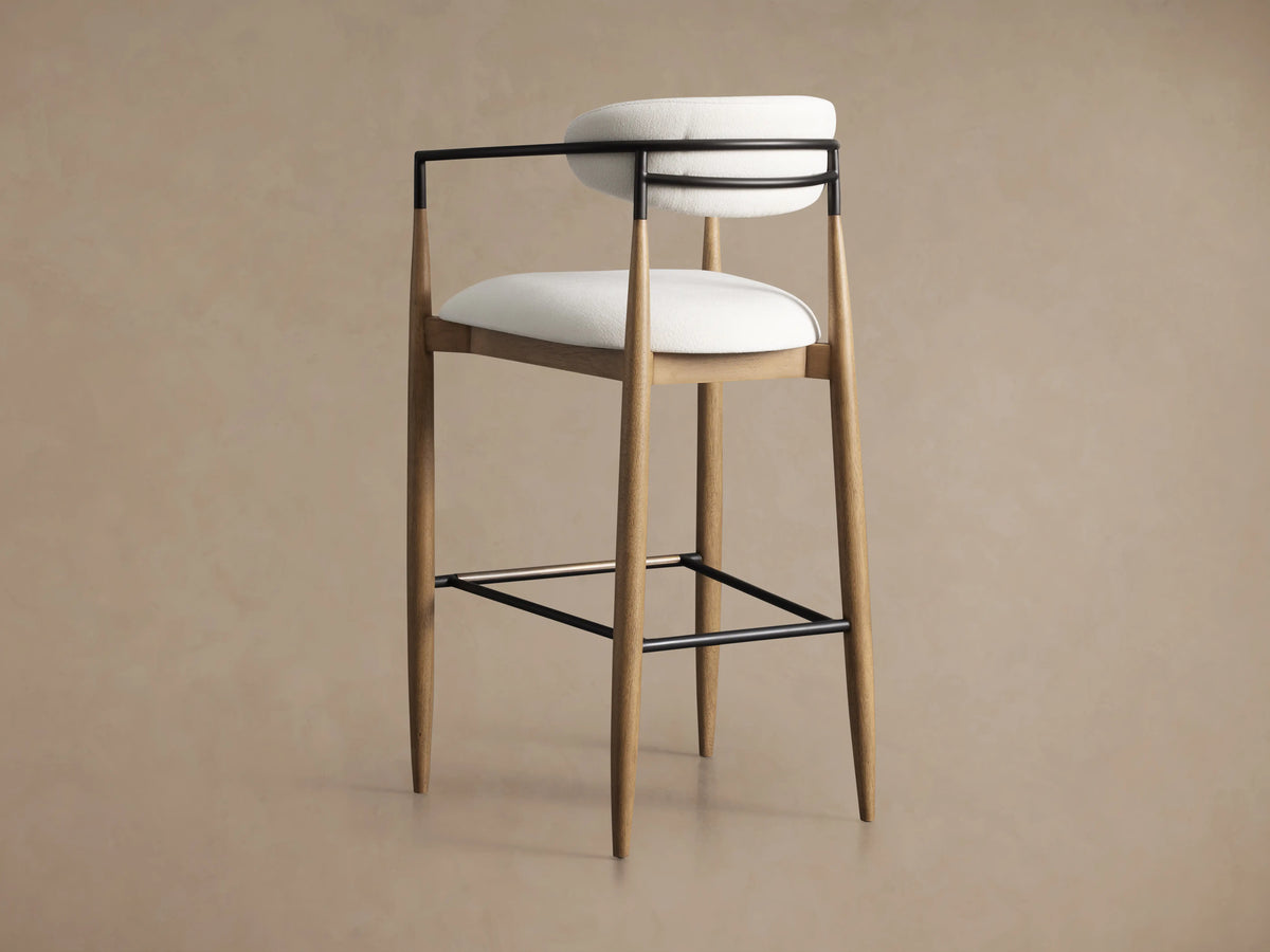Jagger Stool with light wood tapered legs, white upholstered seat and backrest, and black metal armrests and footrest.