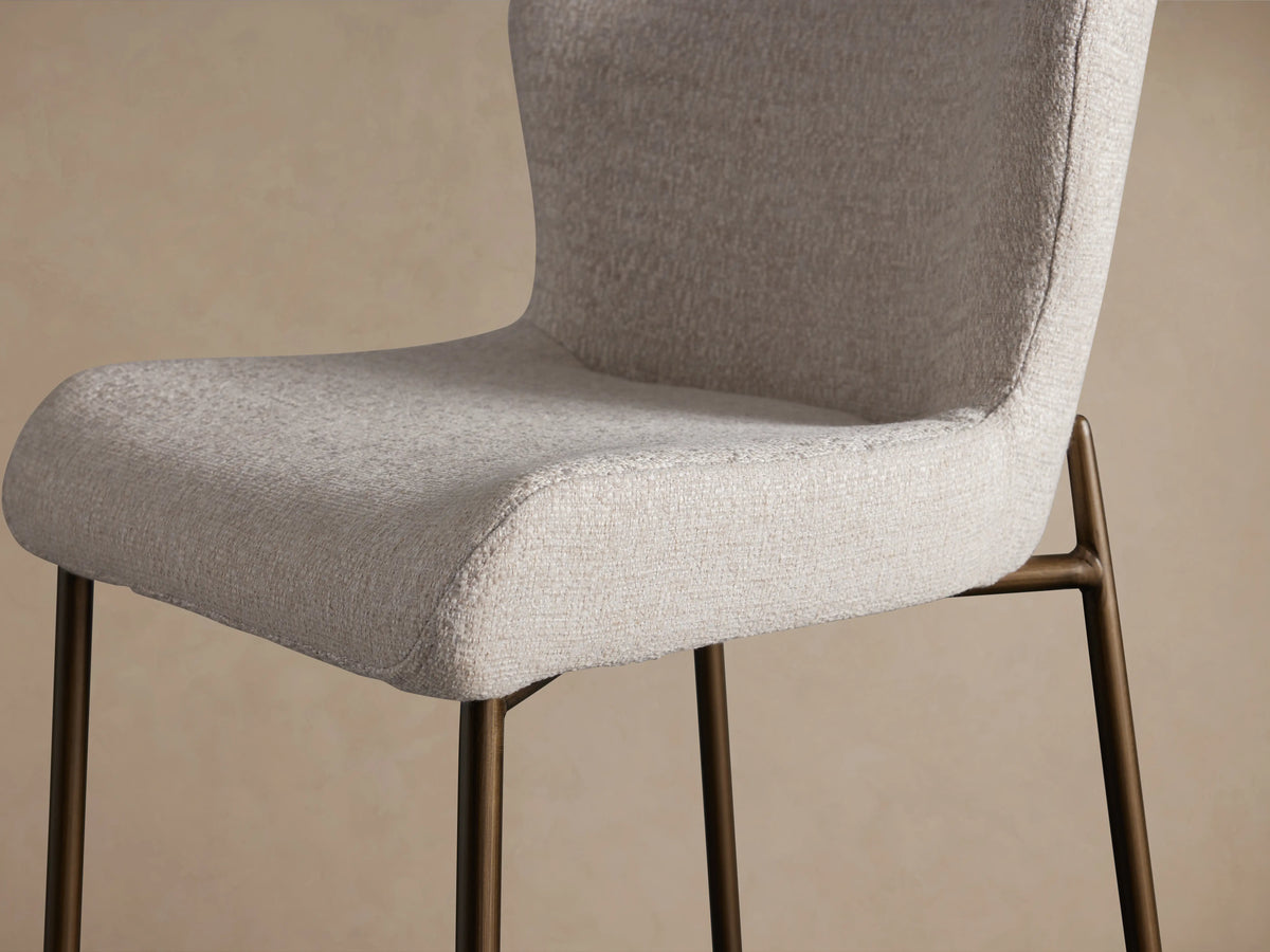 Kirsten Stool in Nona Linen with a curved backrest and cushioned seat, powder-coated iron legs on a wooden floor.