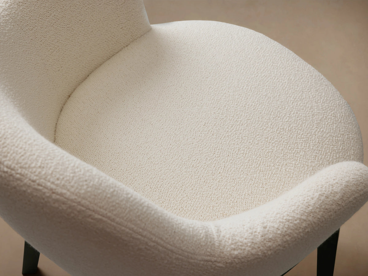 Simone Dining Arm Chair with cream upholstered seat and backrest, dark ash wood frame, on a wood floor, against a beige wall.
