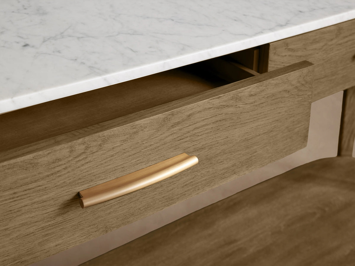 Danny Console Table in oak wood with a light fawn finish, featuring a white marble top and brass drawer pulls, set against a neutral wall.