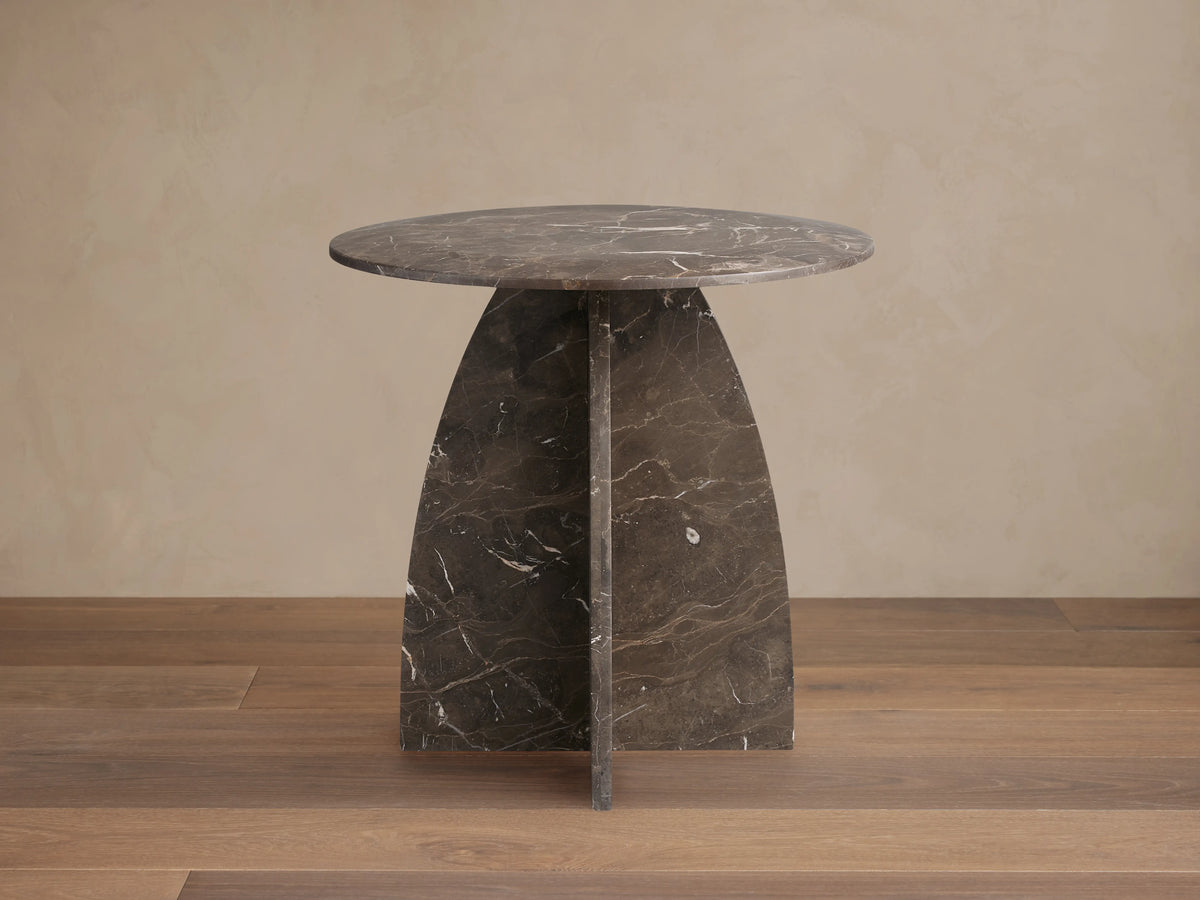 Solstice End Table made of dark marble with a round top and triangular base, showcasing natural white veining, on a wood floor.