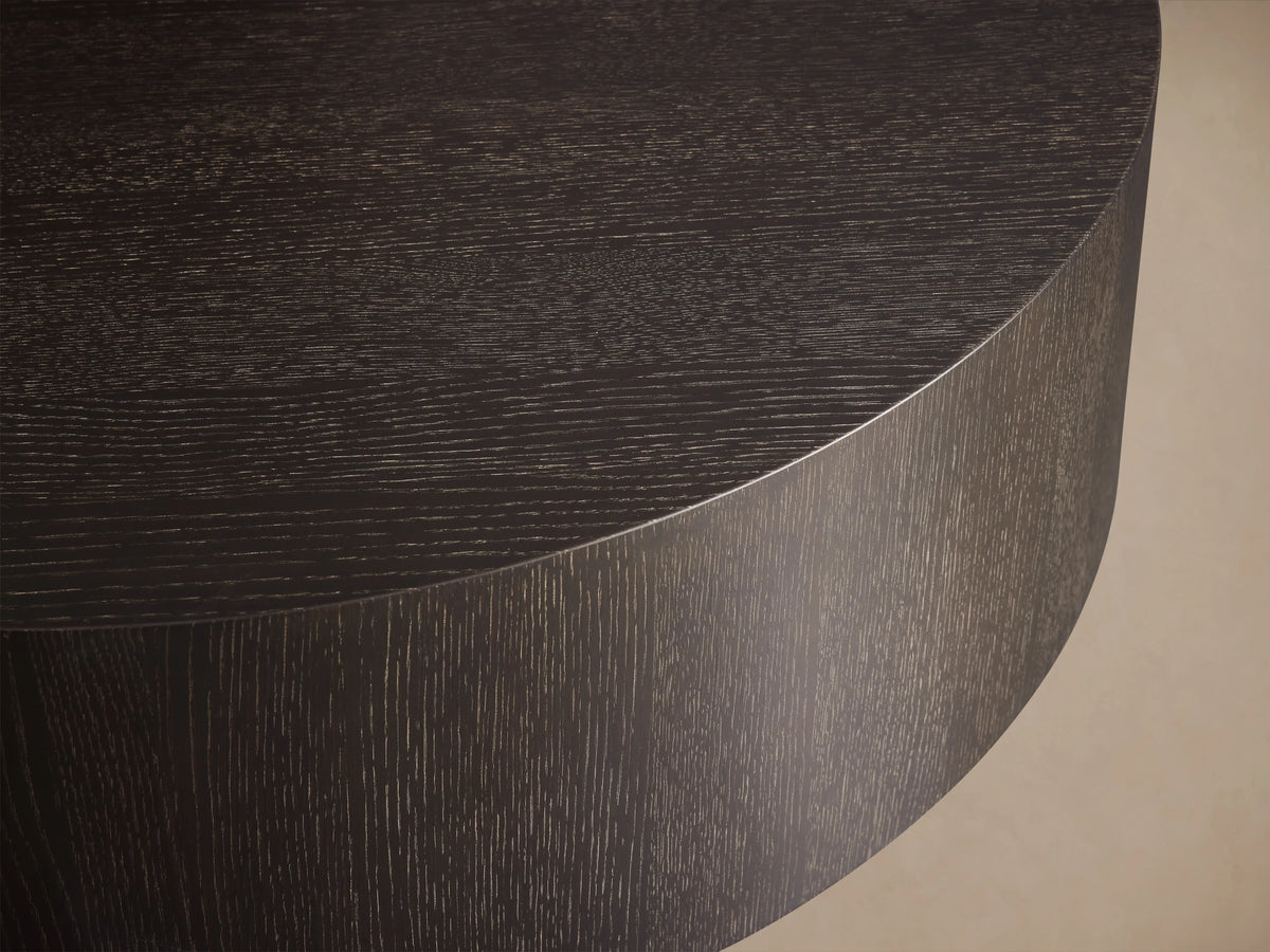 Round wooden coffee table in dark brown Northman Cinder finish, showcasing a smooth top and grained sides on wooden floor.