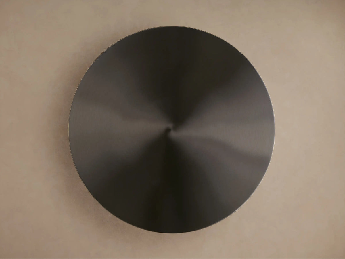 Top-down view of the Urben Martini Table's dark, circular antiqued brass tabletop with a metallic sheen on a light brown background.