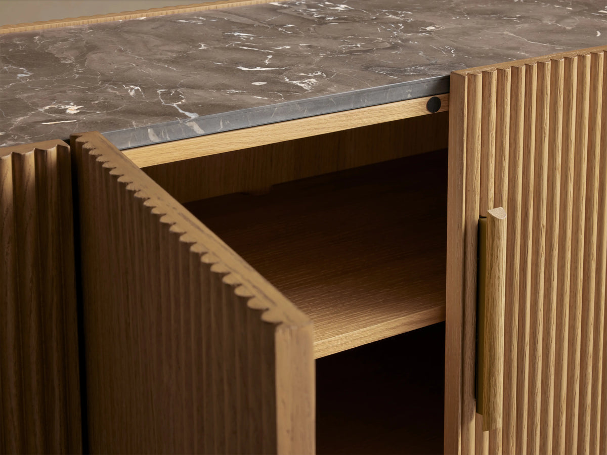 Astor Media Console made of oak with vertical reeding, inset marble top, and a slightly open cabinet door revealing shelves.