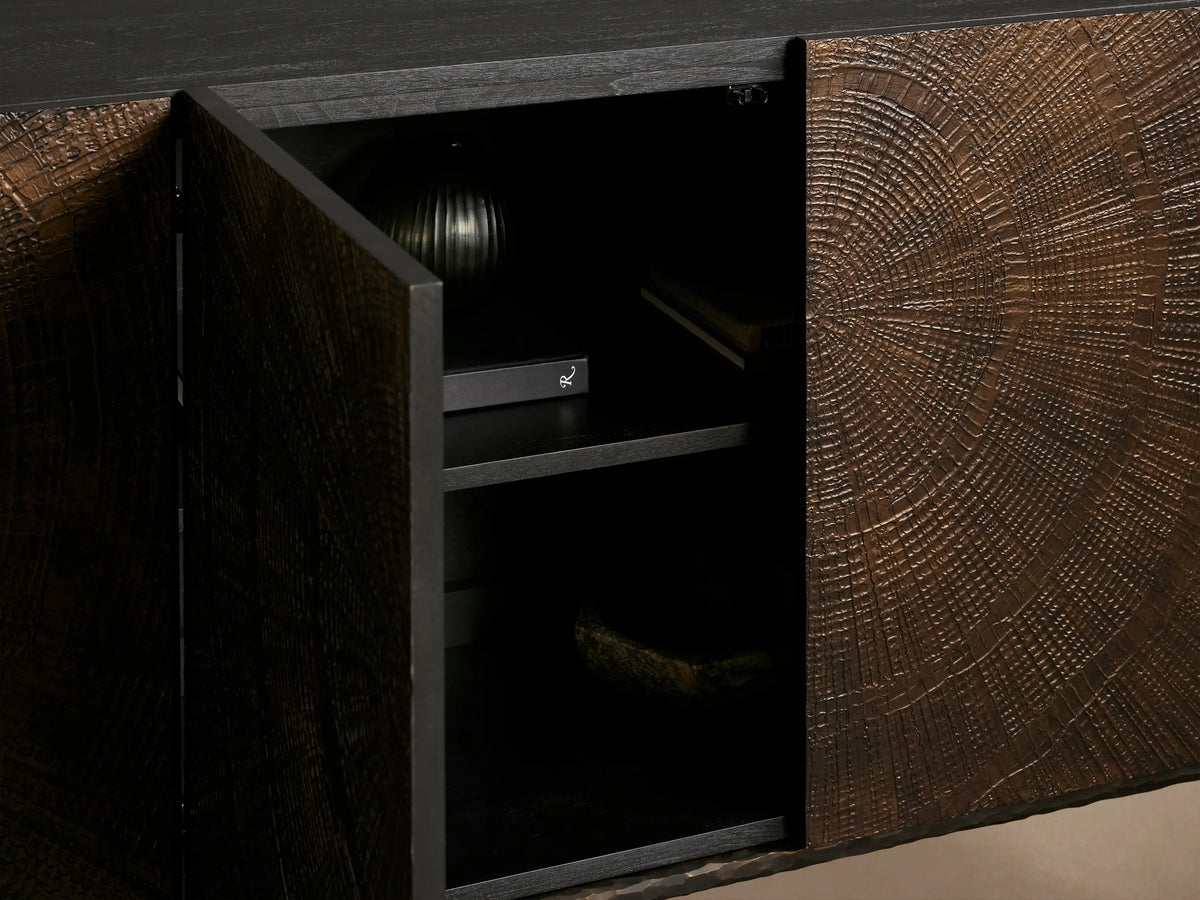 Close-up of Theota Sideboard's dark wood top with visible grain, meeting a textured brown door with a hand-stamped sunburst pattern.