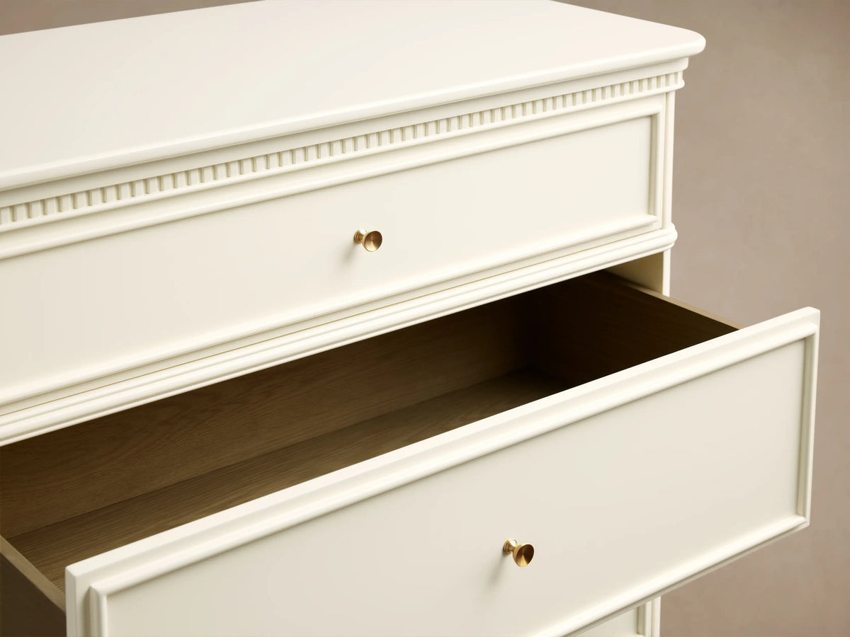 Close-up of the Crv®me Carlisle Five-Drawer Dresser, showing textured molding, an open drawer revealing natural wood interior, and antique brass pulls.