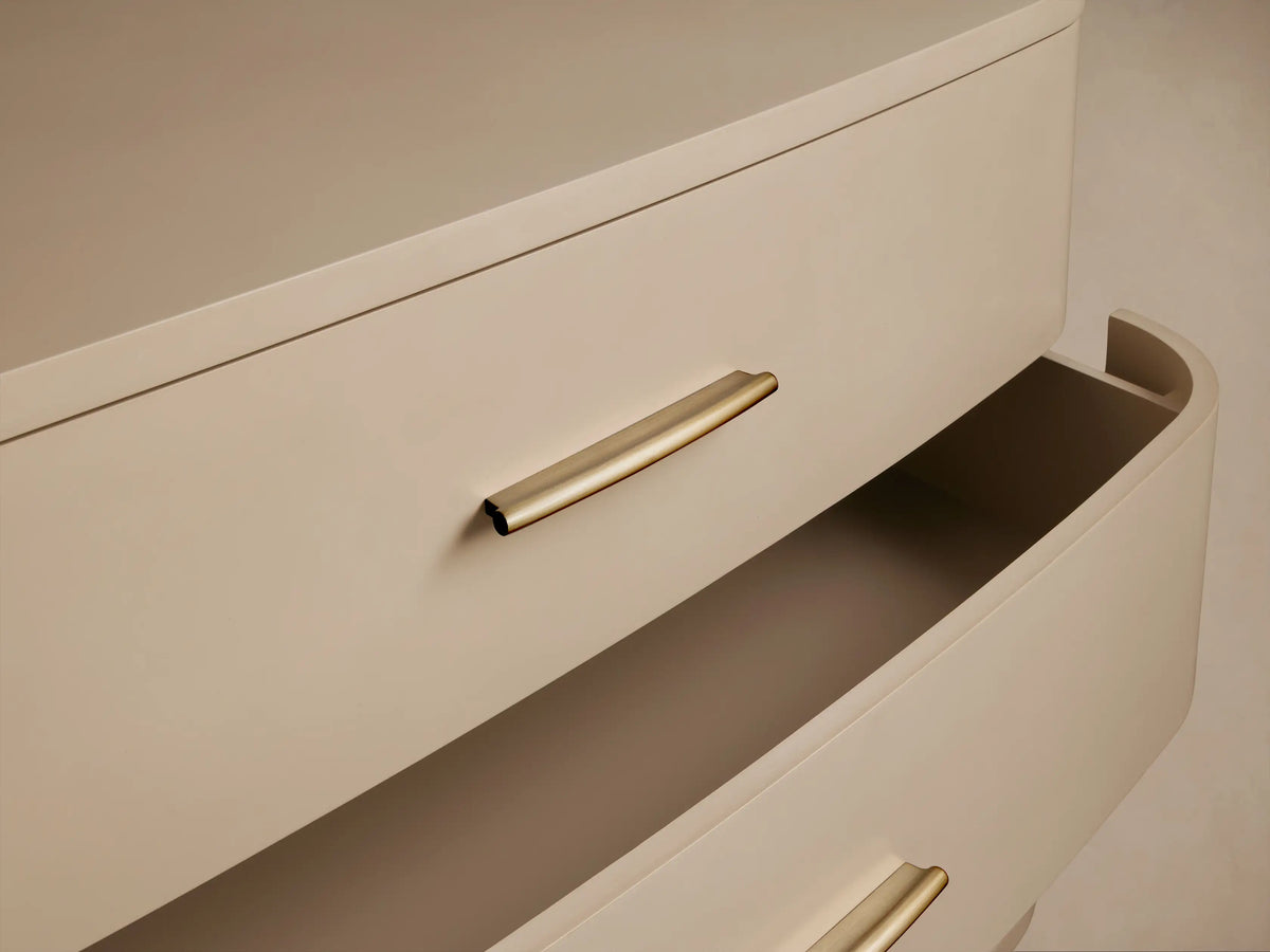 Fumo Danny Six-Drawer Dresser. Light beige, curved front, six drawers with horizontal brass pulls, on splayed legs.