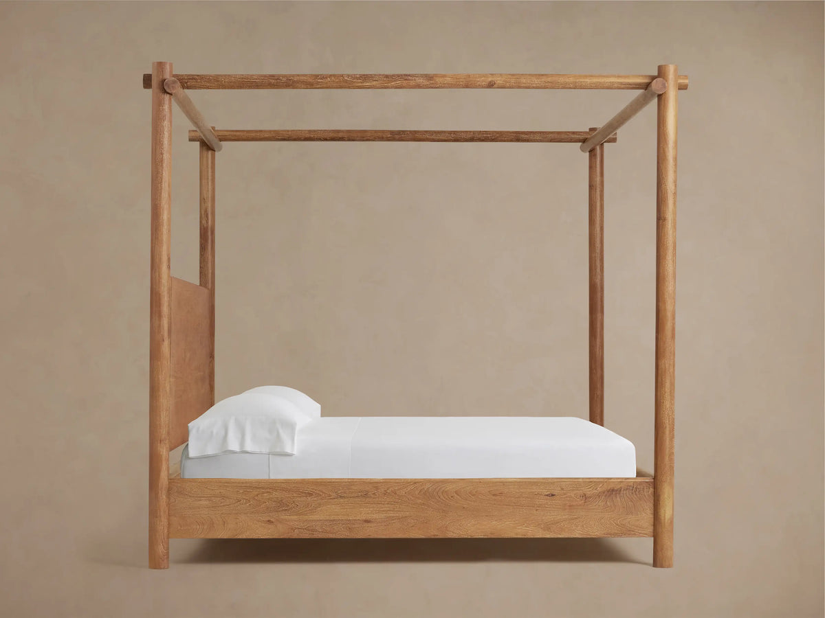 Close-up of Dutton Canopy Bed's acacia wood headboard with Vintage Teak finish, showing rich wood grain next to a rounded canopy post.