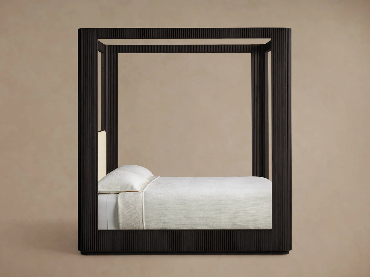 Front view of the Ebony Finnley Canopy Bed, showcasing reeding details, a Latte upholstered headboard, white bedding, and a brown throw.