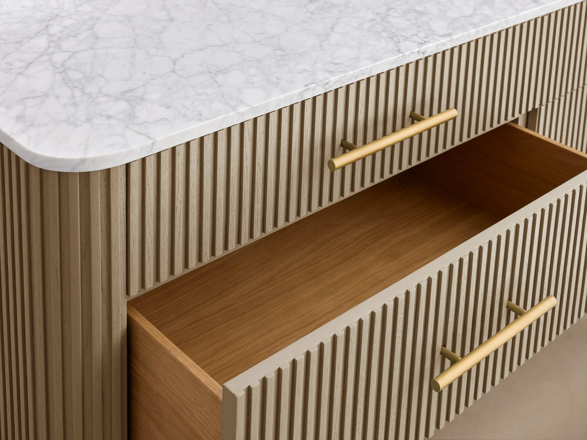 Finnley Six-Drawer Dresser with white marble top, reeded light wood facade, brass bar handles, and angled gold legs.