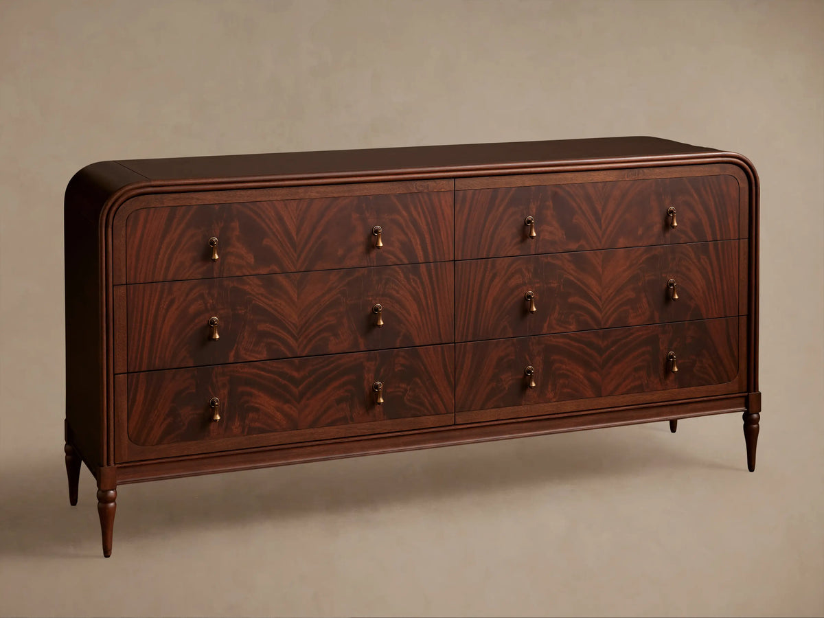 Close-up of Frances Dresser: dark mahogany with curved edges, dramatic figured flame grain. Vintage brass pull, one drawer slightly open.