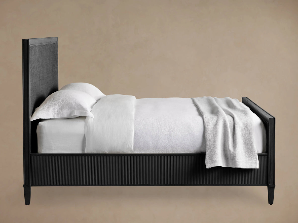 Dark-stained Pearson Cane Bed with textured cane headboard & footboard, dressed in white, on a wooden floor.