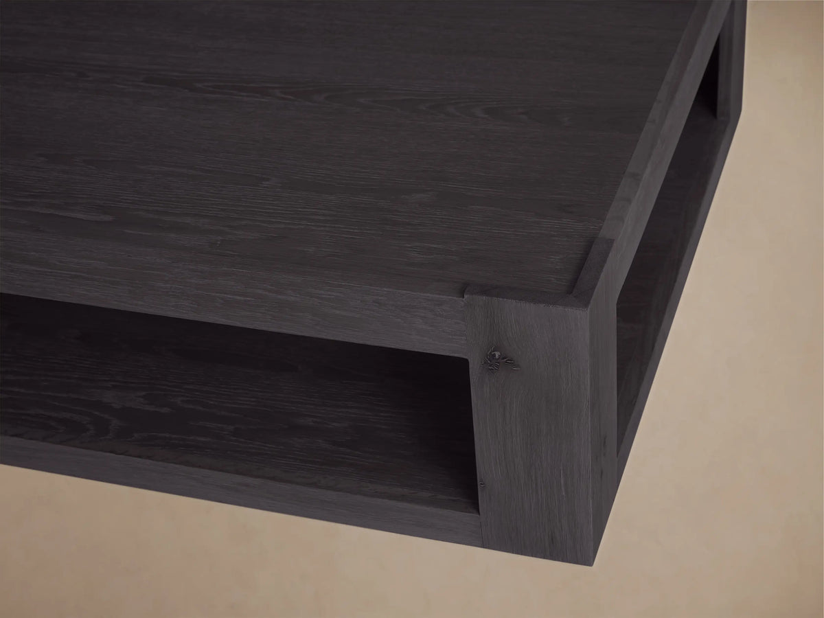 Black oak Devon Coffee Table, rectangular with a lower shelf, angled on wood floor against a beige wall.