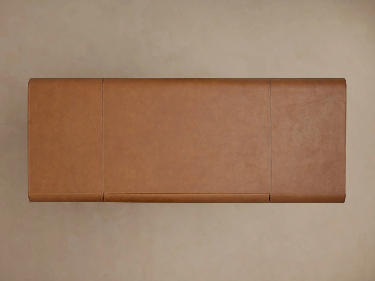 Brown leather corner of the Tullson Leather Desk with visible stitching, set on a brass base, against a beige background.