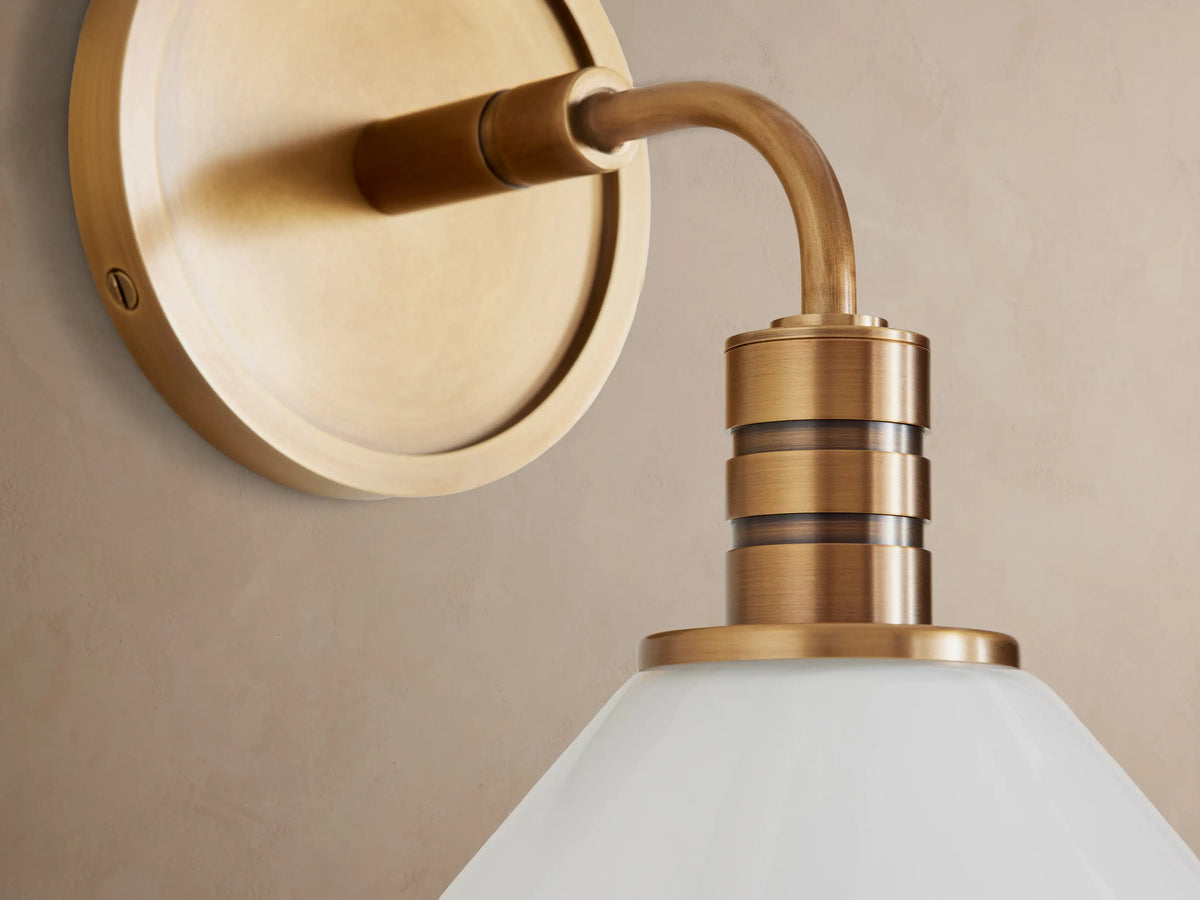 Theron Sconce: Brass wall light with round backplate, arched arm, and white milk glass cone shade pointing down.