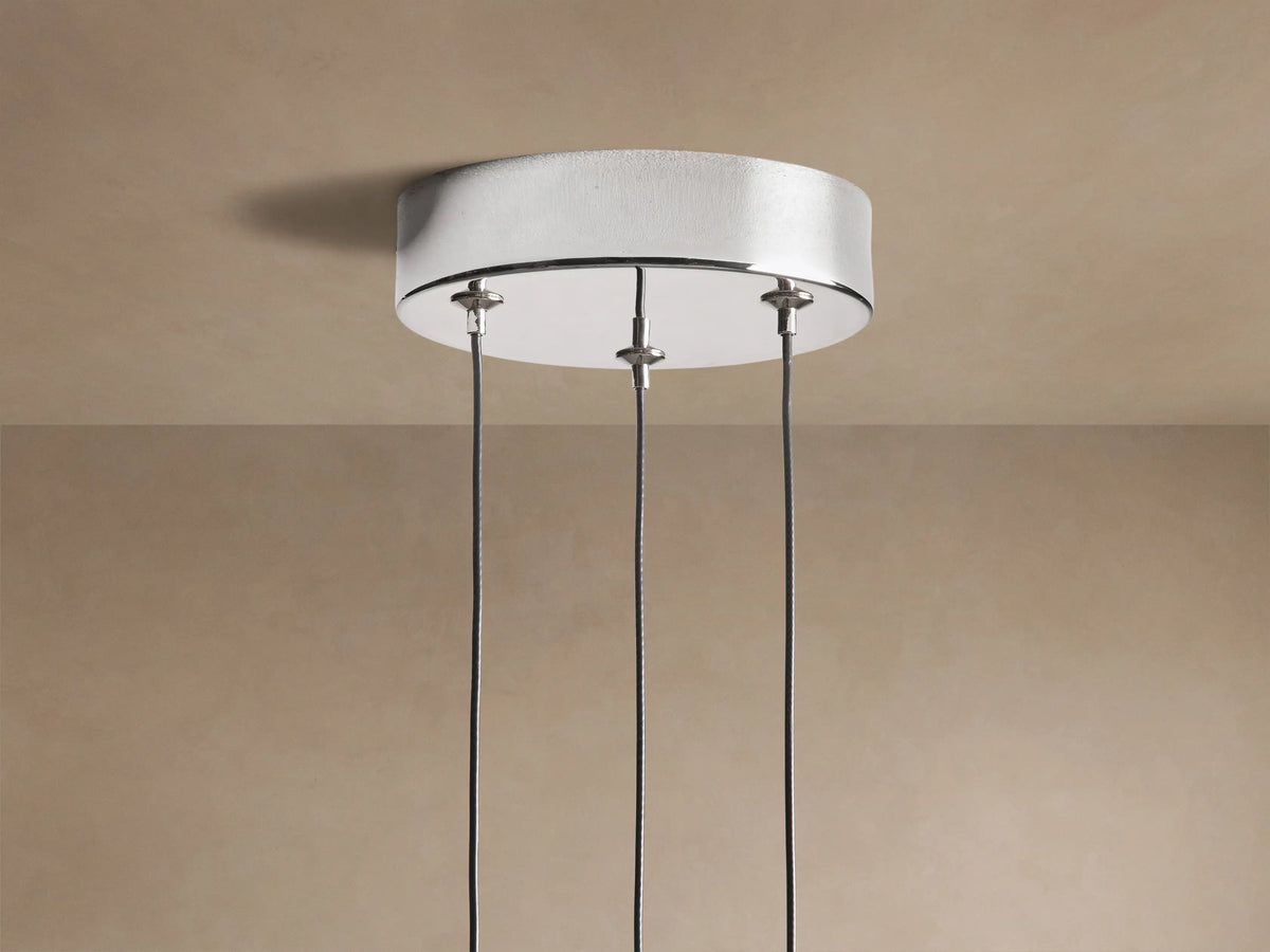 Three illuminated Soltaire Cluster Pendants with clear bubbled glass and polished nickel caps, hanging against a beige wall.
