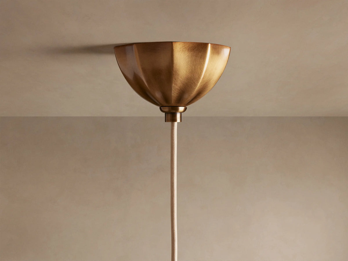 Close-up of Agnes Pendant with antique brass scalloped top, ribbed suspension, and glowing, wavy cream glass shade.