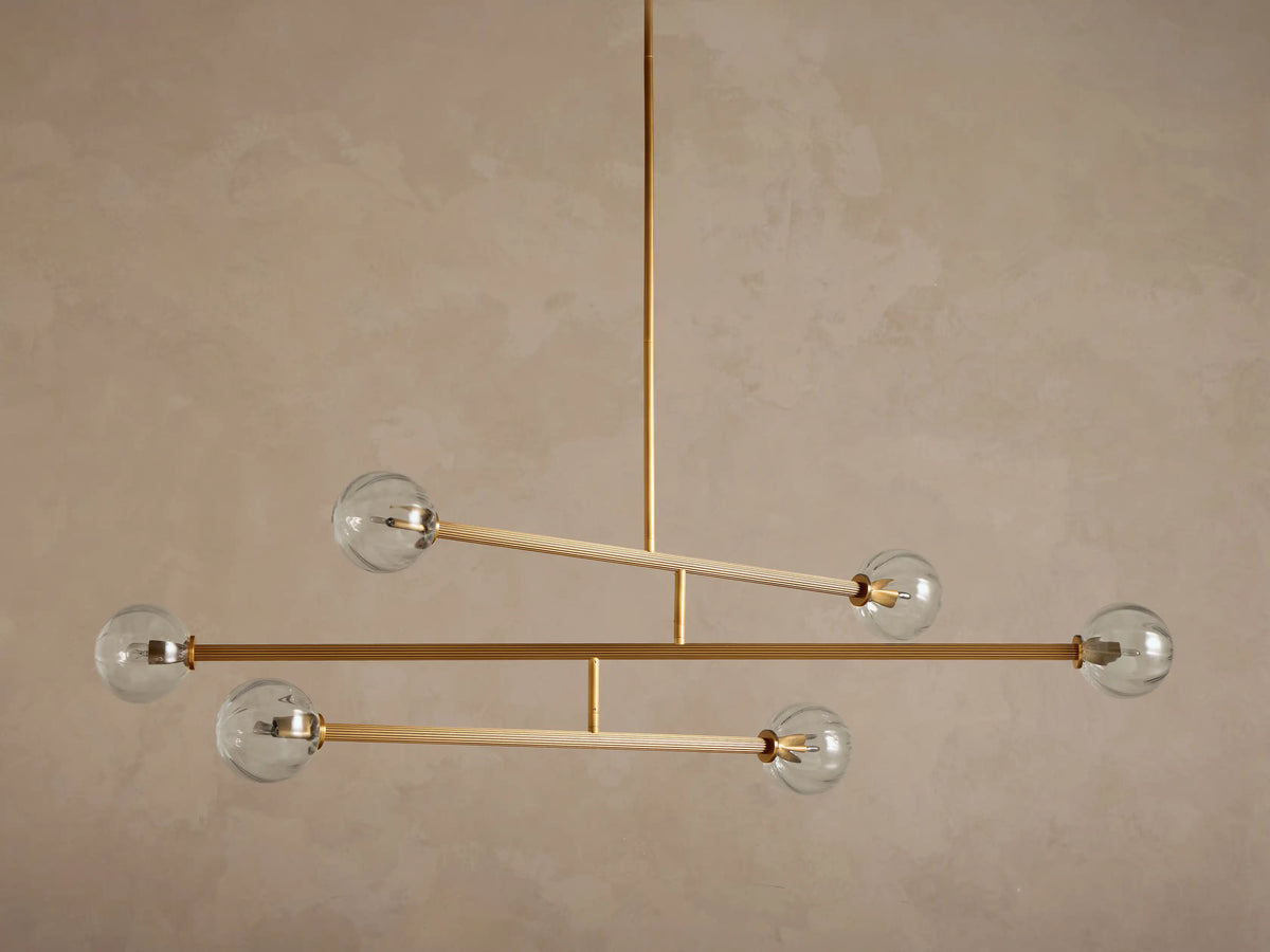 Front view of modern chandelier with illuminated clear glass ribbed globes and brass-toned metal arms.