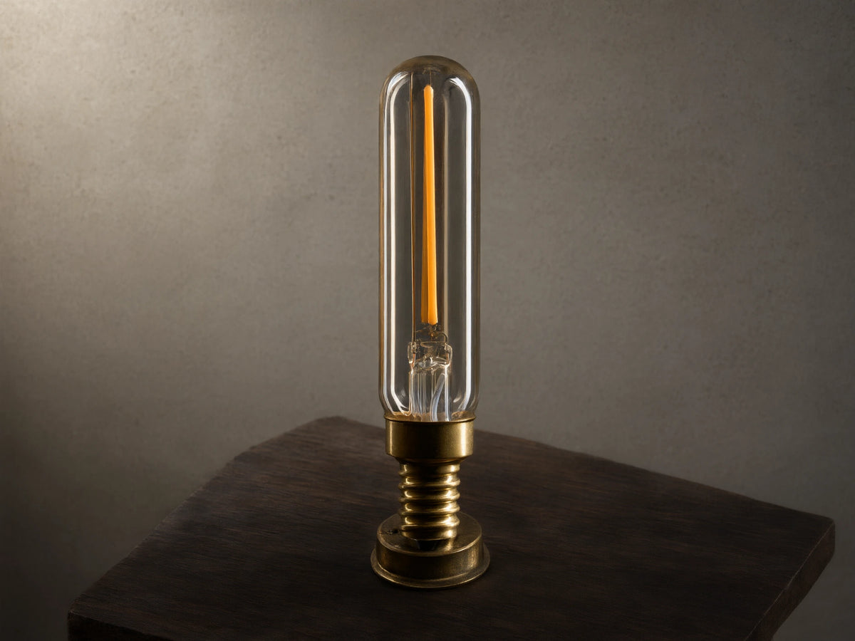 A tubular LED filament bulb with a clear glass casing and a brass base, illuminated against a black background.