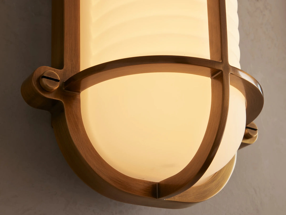 Solomon Outdoor Sconce with a brass frame and ribbed white milk glass diffuser, mounted vertically on a light beige wall.