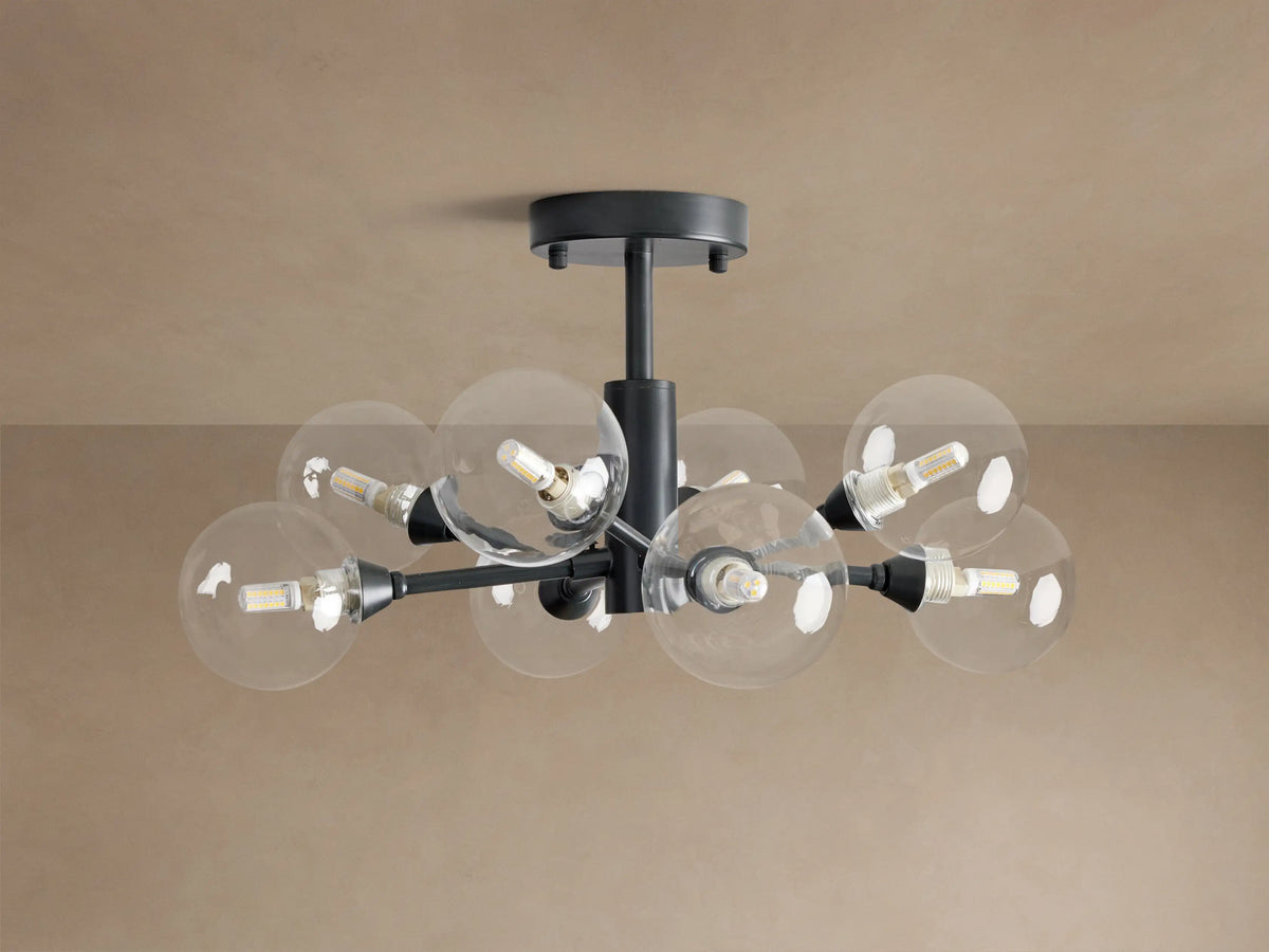Apollo Flush Mount, dark metal, with eight clear spherical bulbs glowing. Mounted on a light brown ceiling.