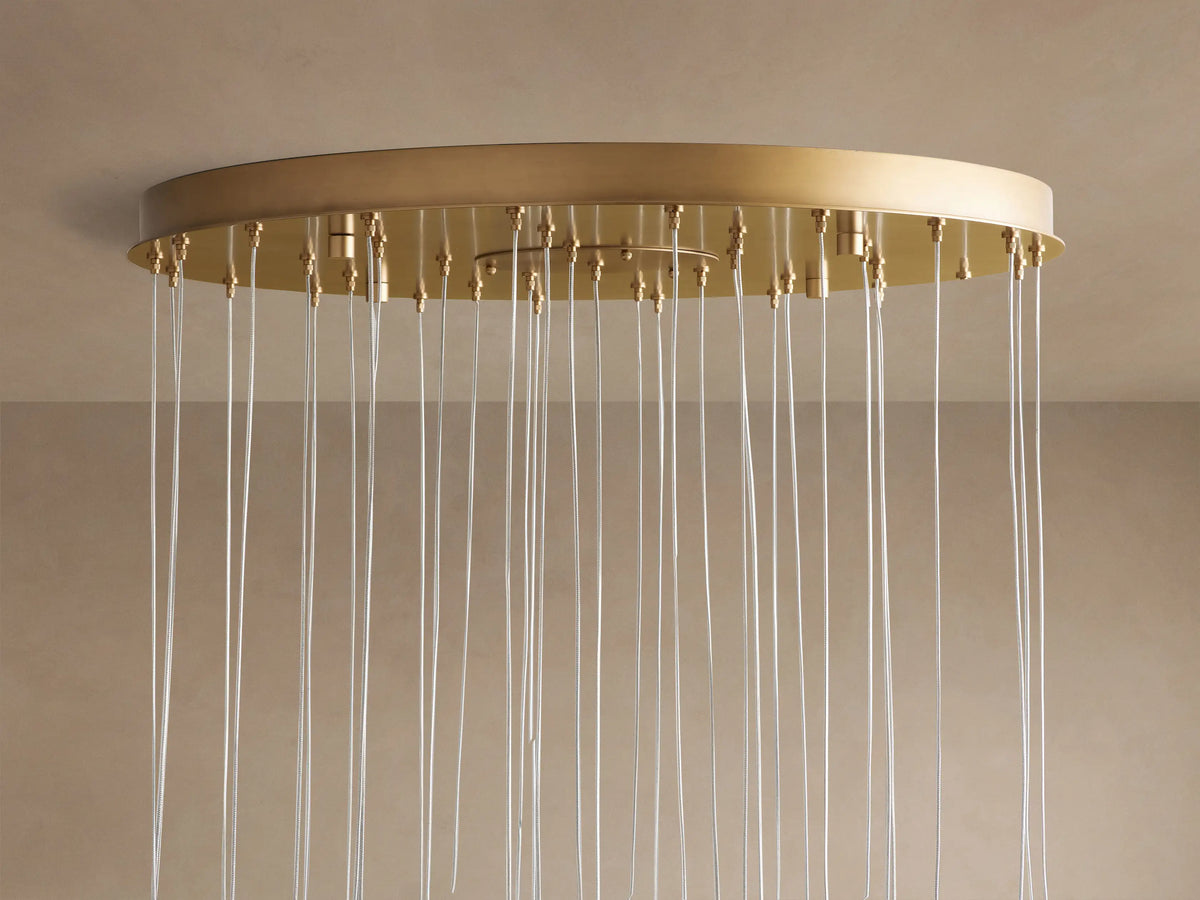 Arica Round Chandelier: circular gold canopy mounted to a beige ceiling, with many clear airplane cables hanging down.