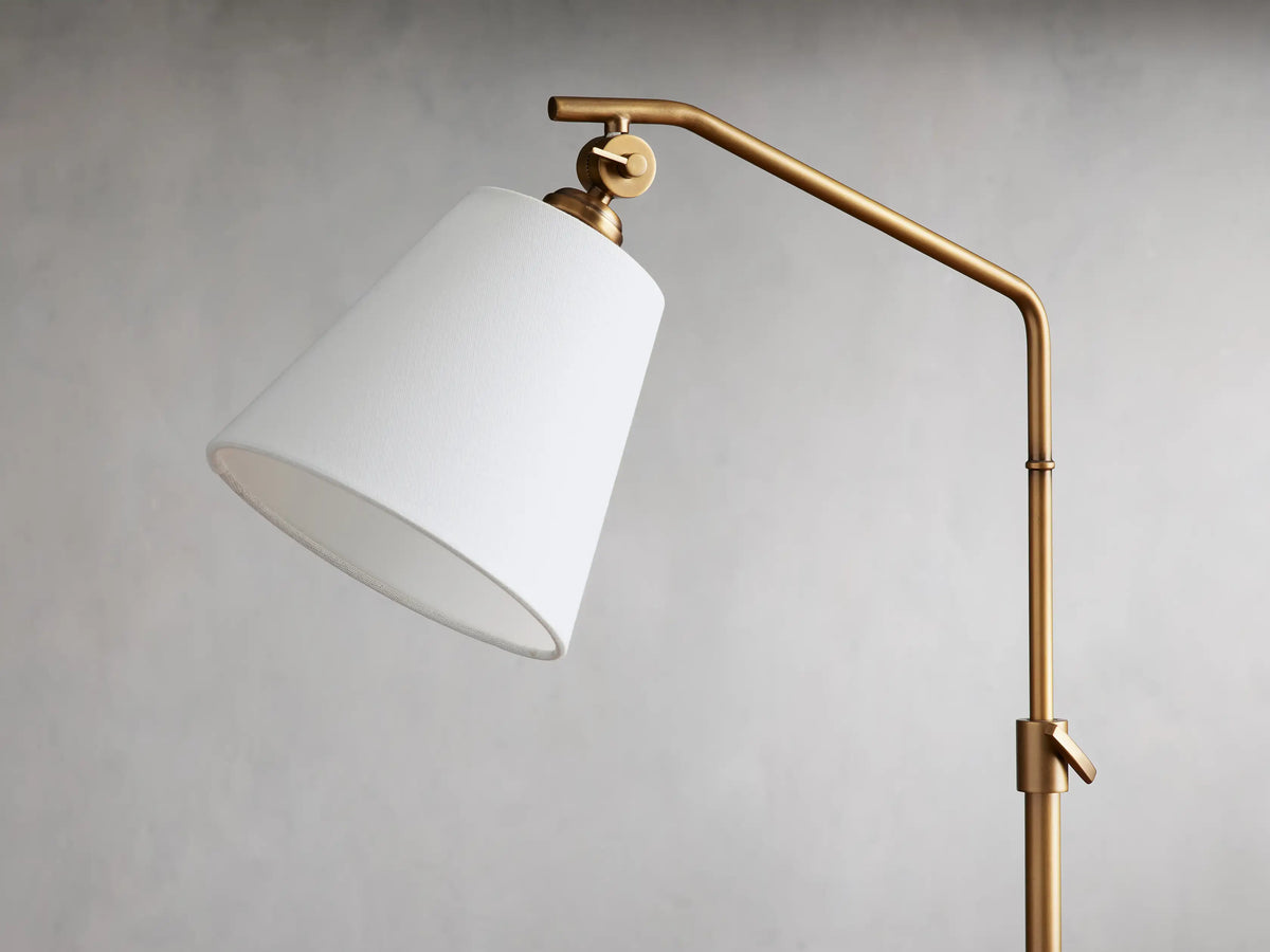 Kellen Table Lamp with an antiqued-brass frame, white linen shade, adjustable height on wooden table, simple design.
