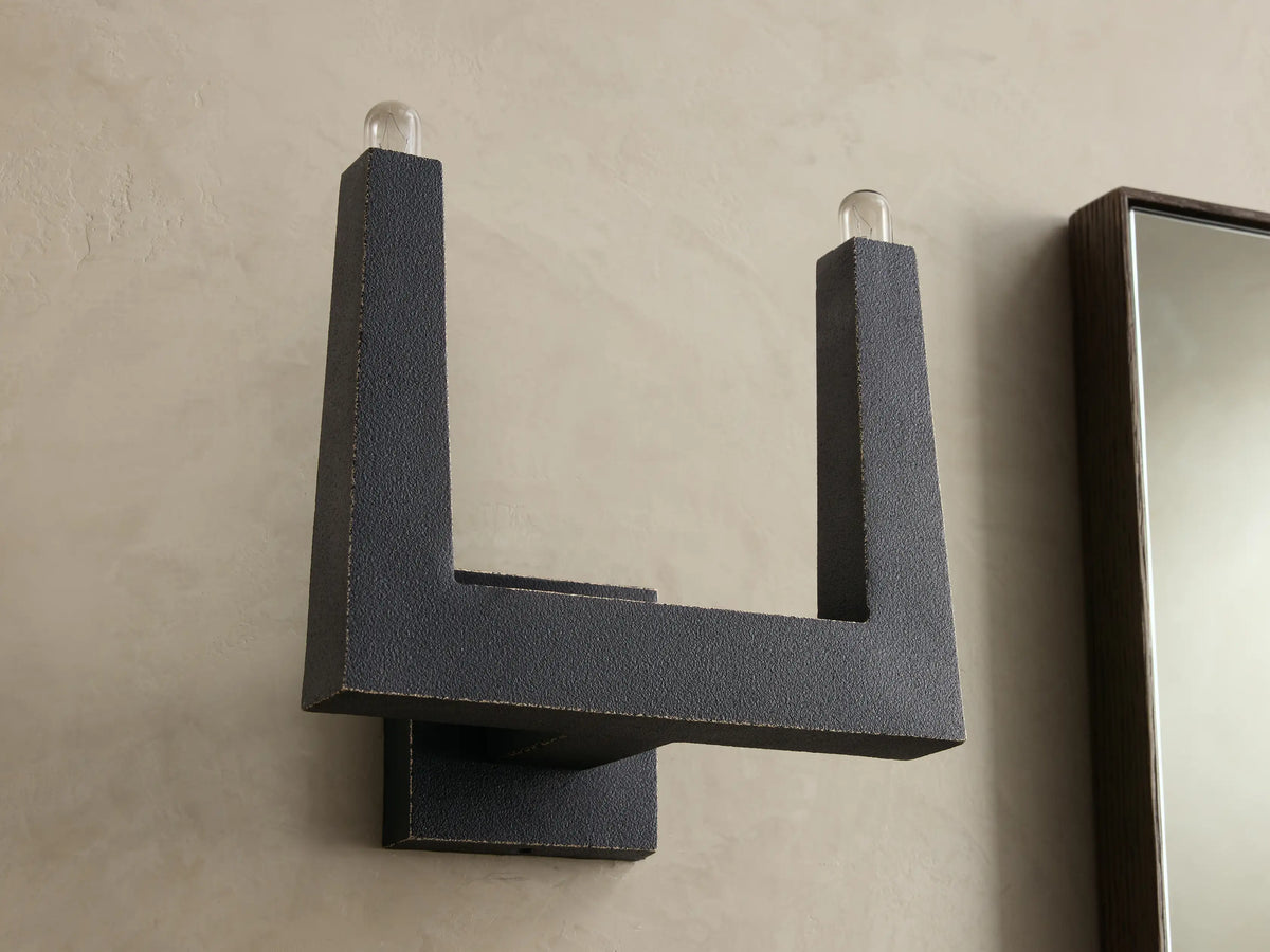 Front view of a dark gray textured U-shaped wall sconce with two clear glass bulbs at the top.
