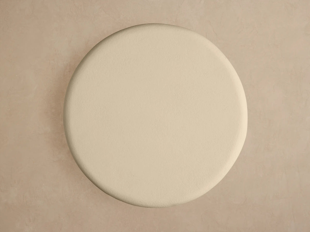 Close-up of Anami Outdoor End Table. Round, cream textured top on a light, curved teak wood base with visible grain.