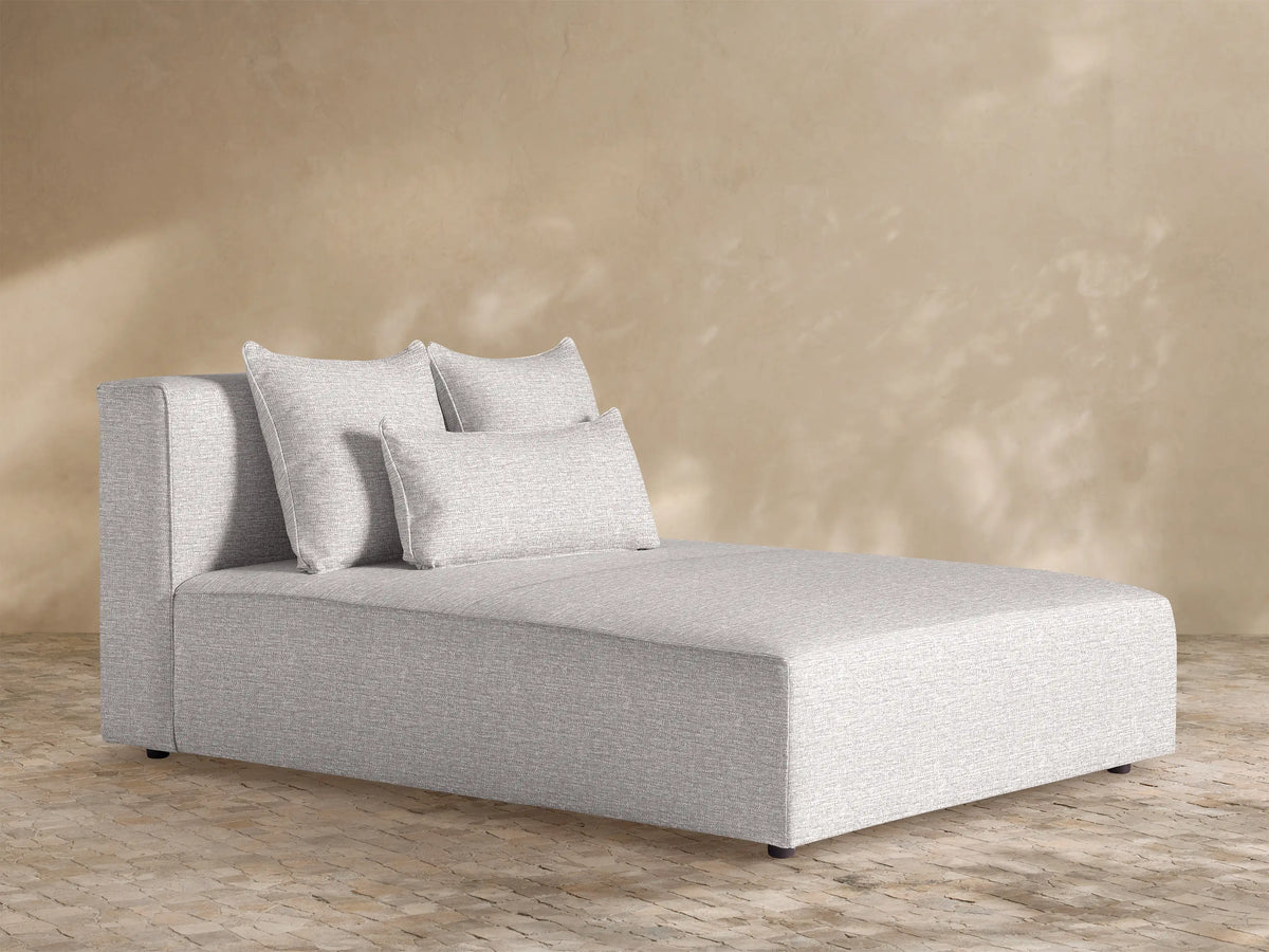 Light gray textured Andaz Outdoor Chaise, modern, blocky design, with two square and one kidney pillow, against a beige wall.