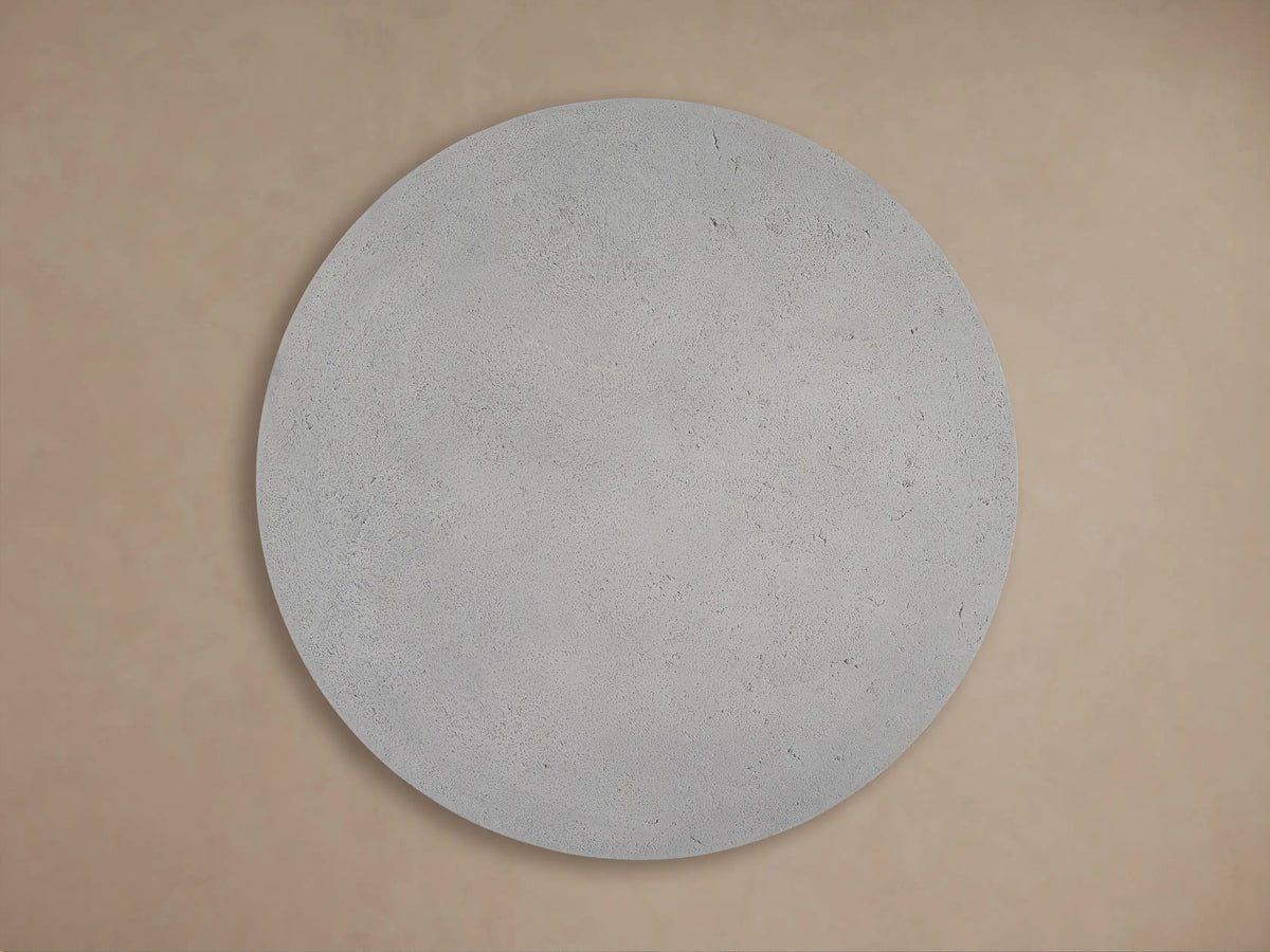 Angled close-up of Azores Round Coffee Table's light gray, textured faux travertine top and edge, with shadows.
