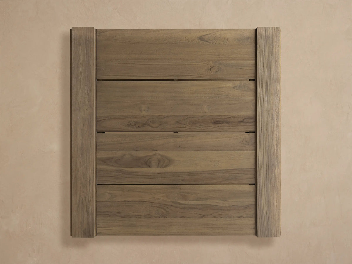 Canyon Outdoor Teak Coffee Table. Square, weathered teak with slatted top & lower shelf, on a rustic tiled patio.
