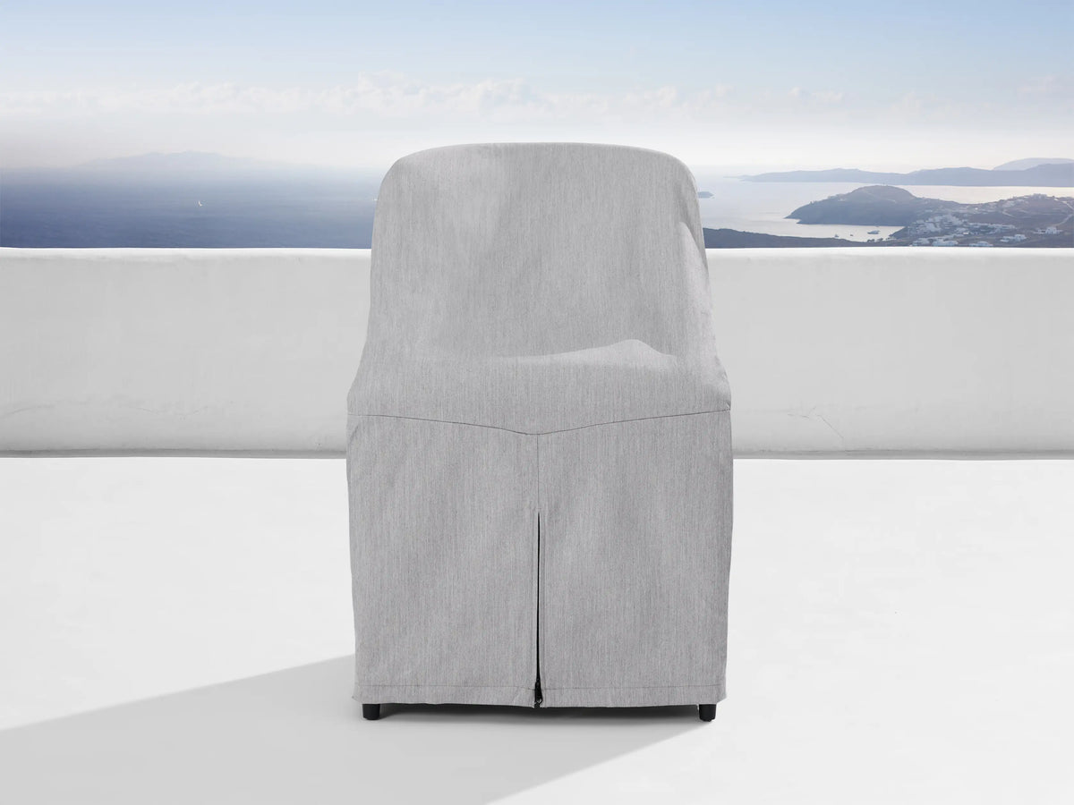 Jagger Outdoor Dining Side Chair, natural teak frame, light beige cushions, on a white patio overlooking a blue sea & islands.