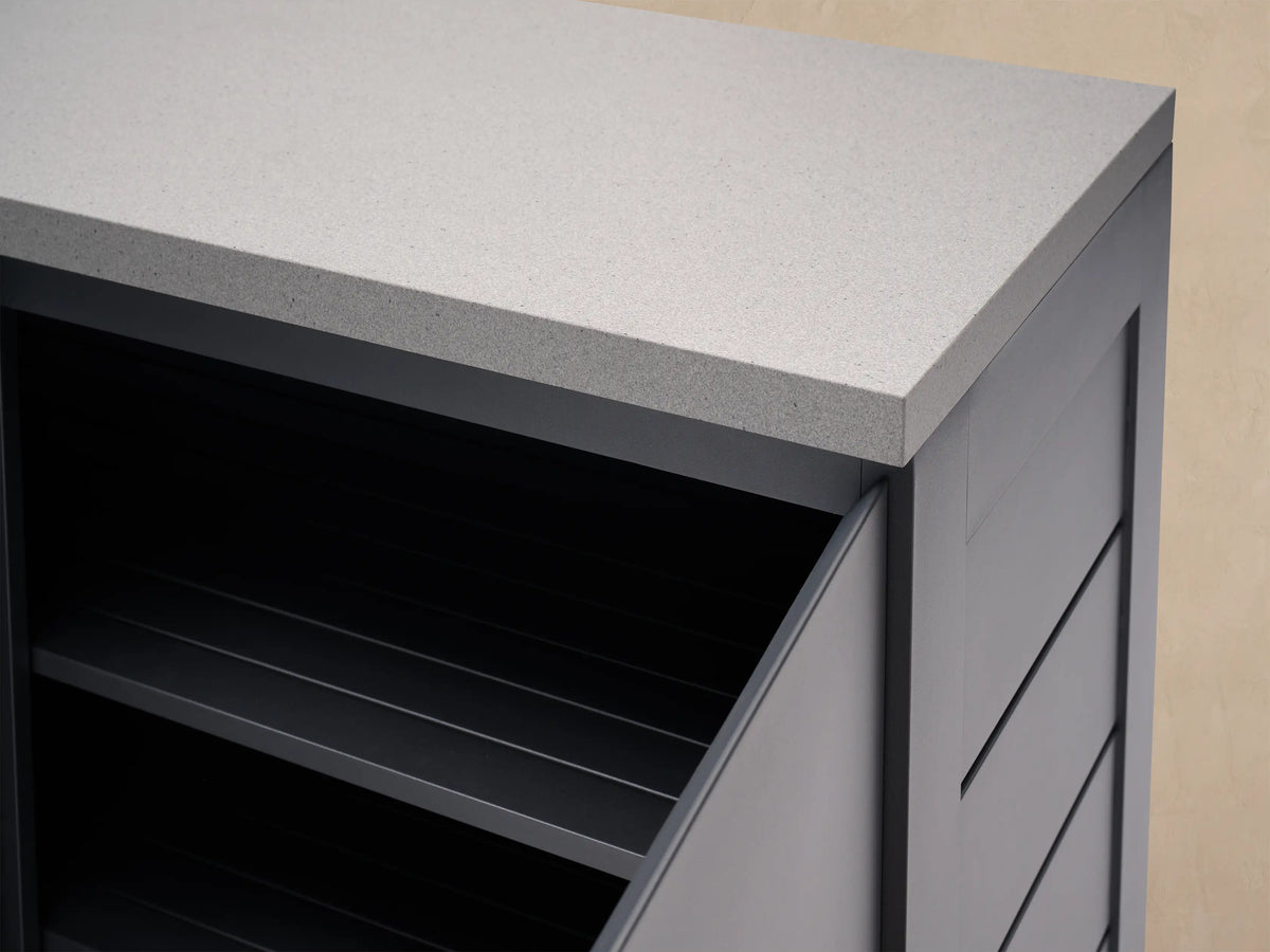 Dark gray outdoor aluminum modular corner kitchen cabinet with light gray stone top. Left door open, right slatted.
