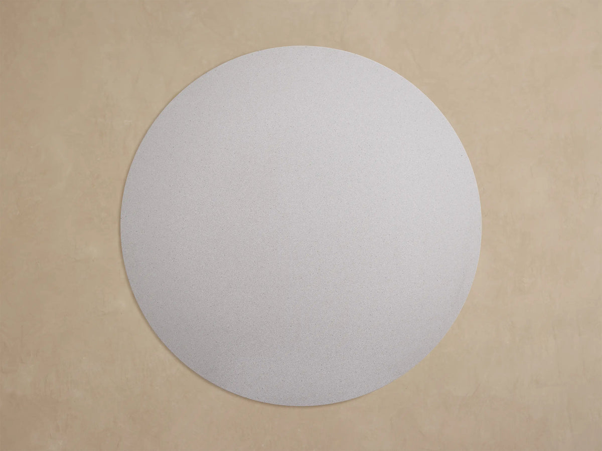 Close-up of a light gray speckled round Outdoor Dining Table, showing its thick edge and a dark gray angular Apex base leg.