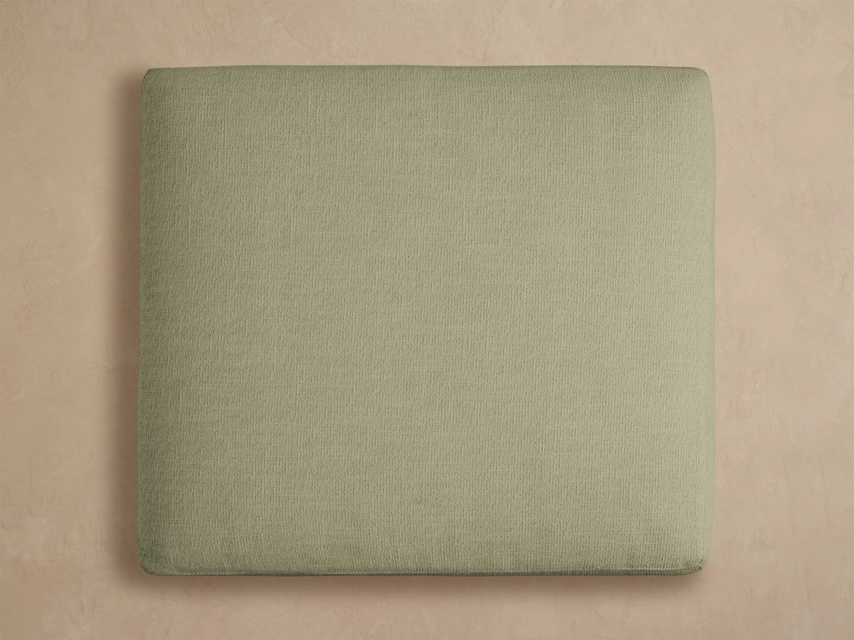 Montego Outdoor Aluminum Ottoman, close-up. Eden Sage fabric cushion with woven texture, resting on a black aluminum frame.